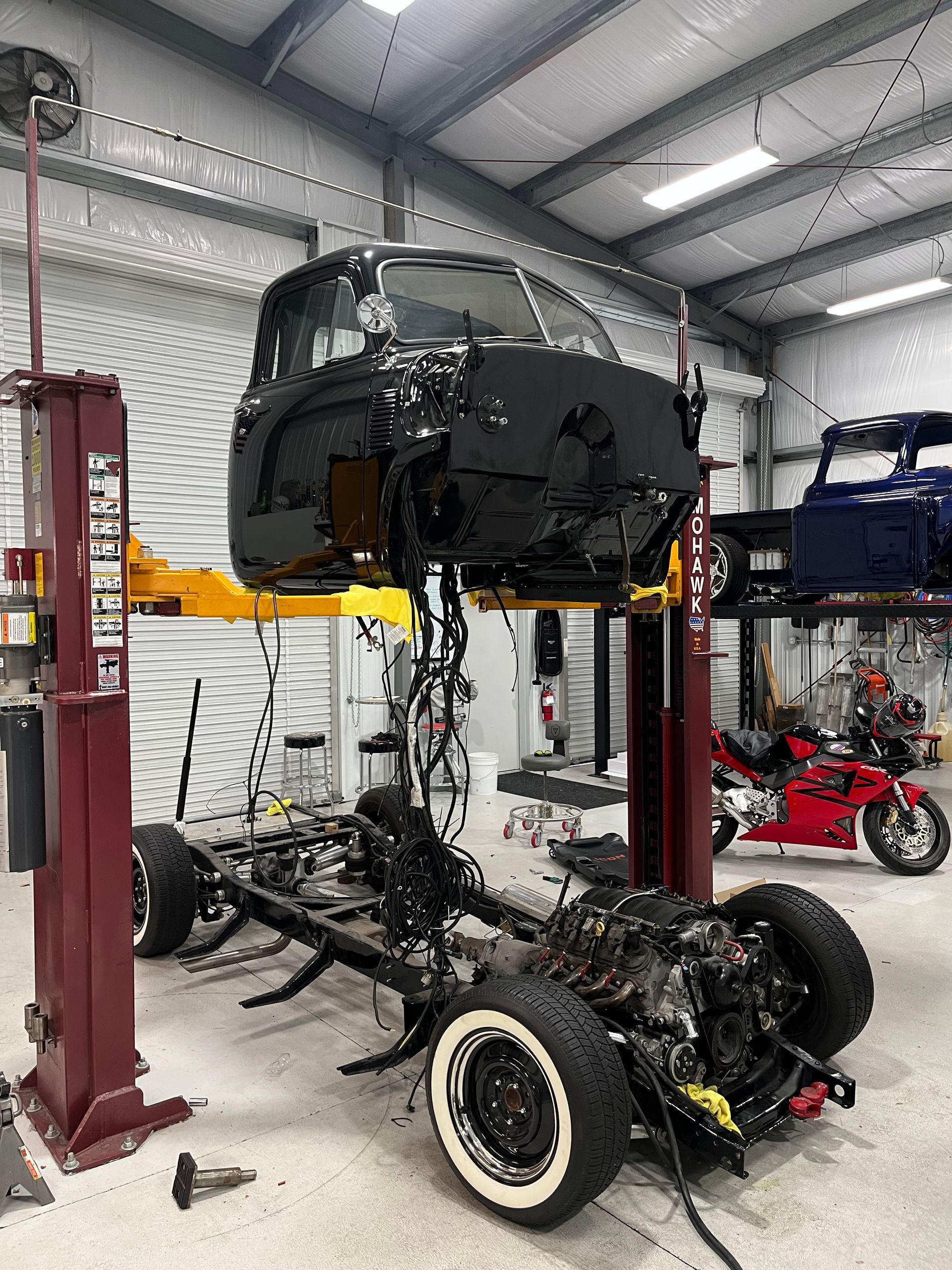 Car body lifted on a red hoist above a disassembled chassis in an auto repair shop
