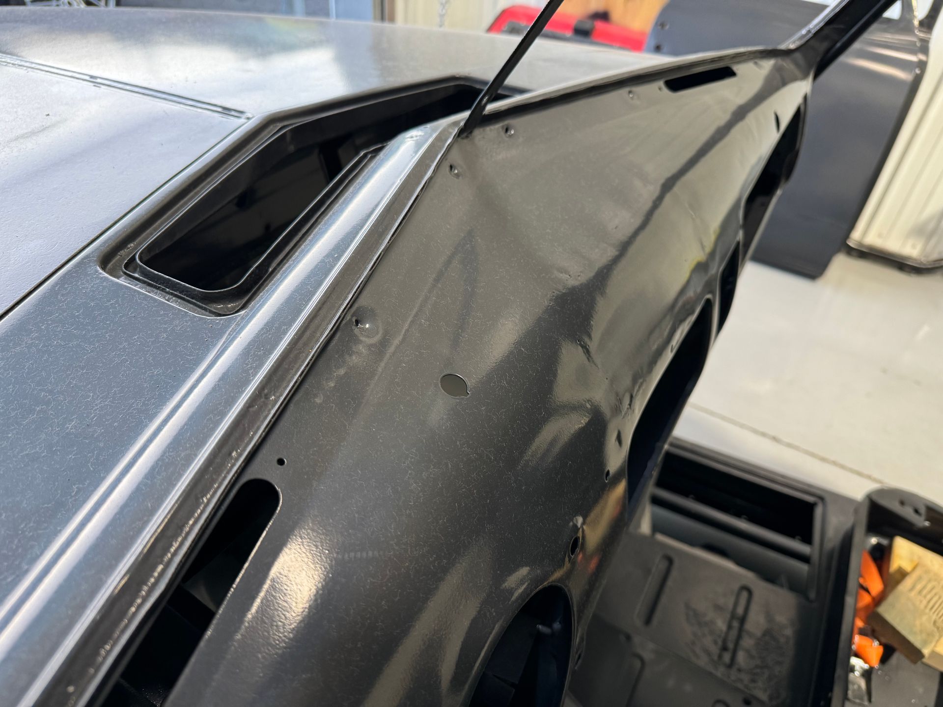 Close-up of a damaged black car body panel with a dented, bent edge in a garage