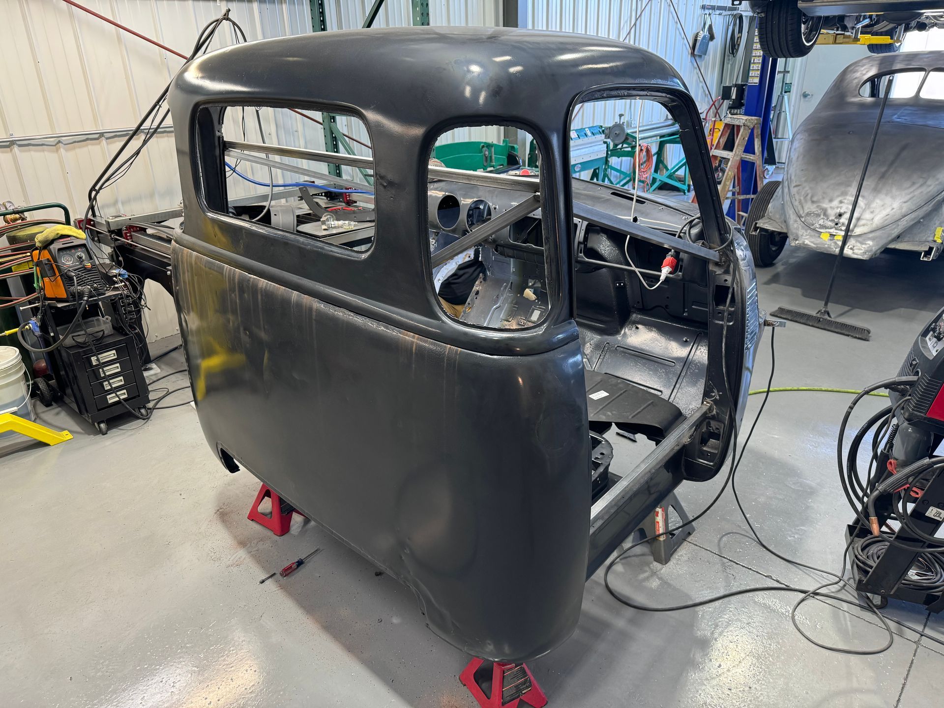 Black hot rod body shell in an auto shop, with windows open and tools in the background