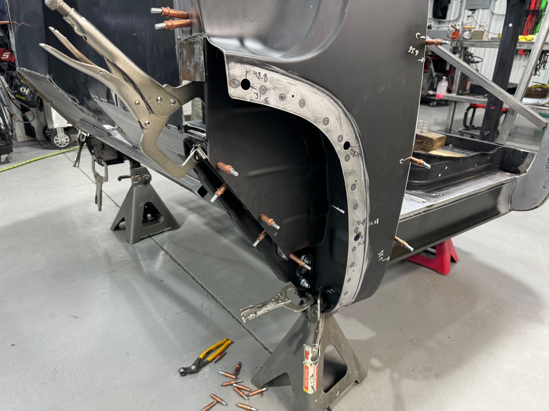 Damaged car body with exposed frame and tools in a repair shop, held by clamps and supports