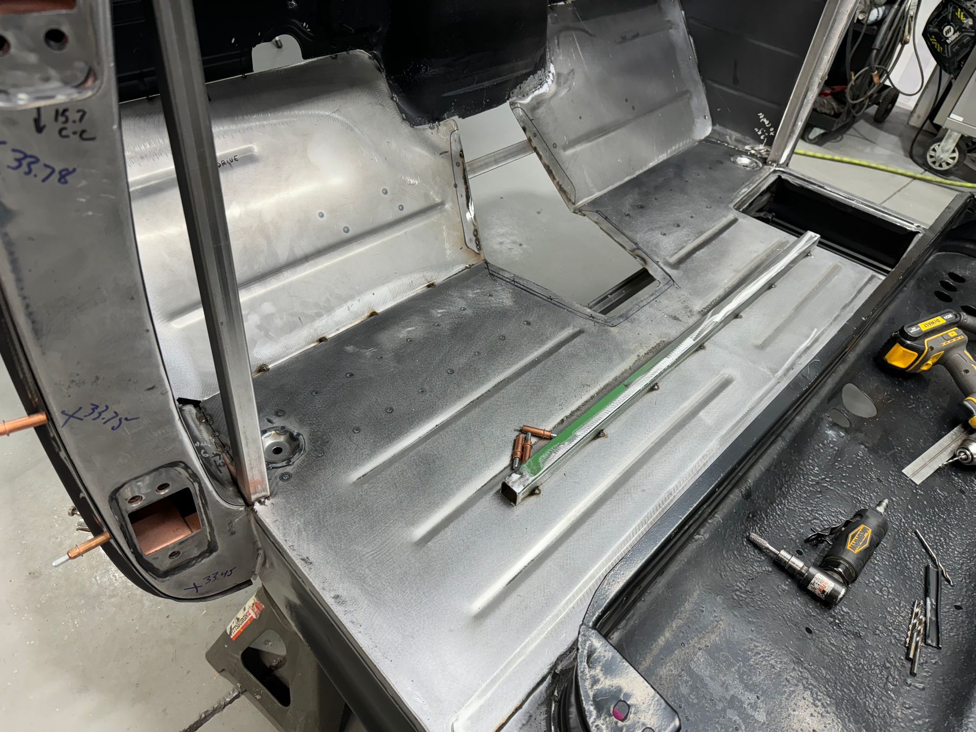 Interior of a bare metal vehicle shell with exposed wiring and tools on the floor