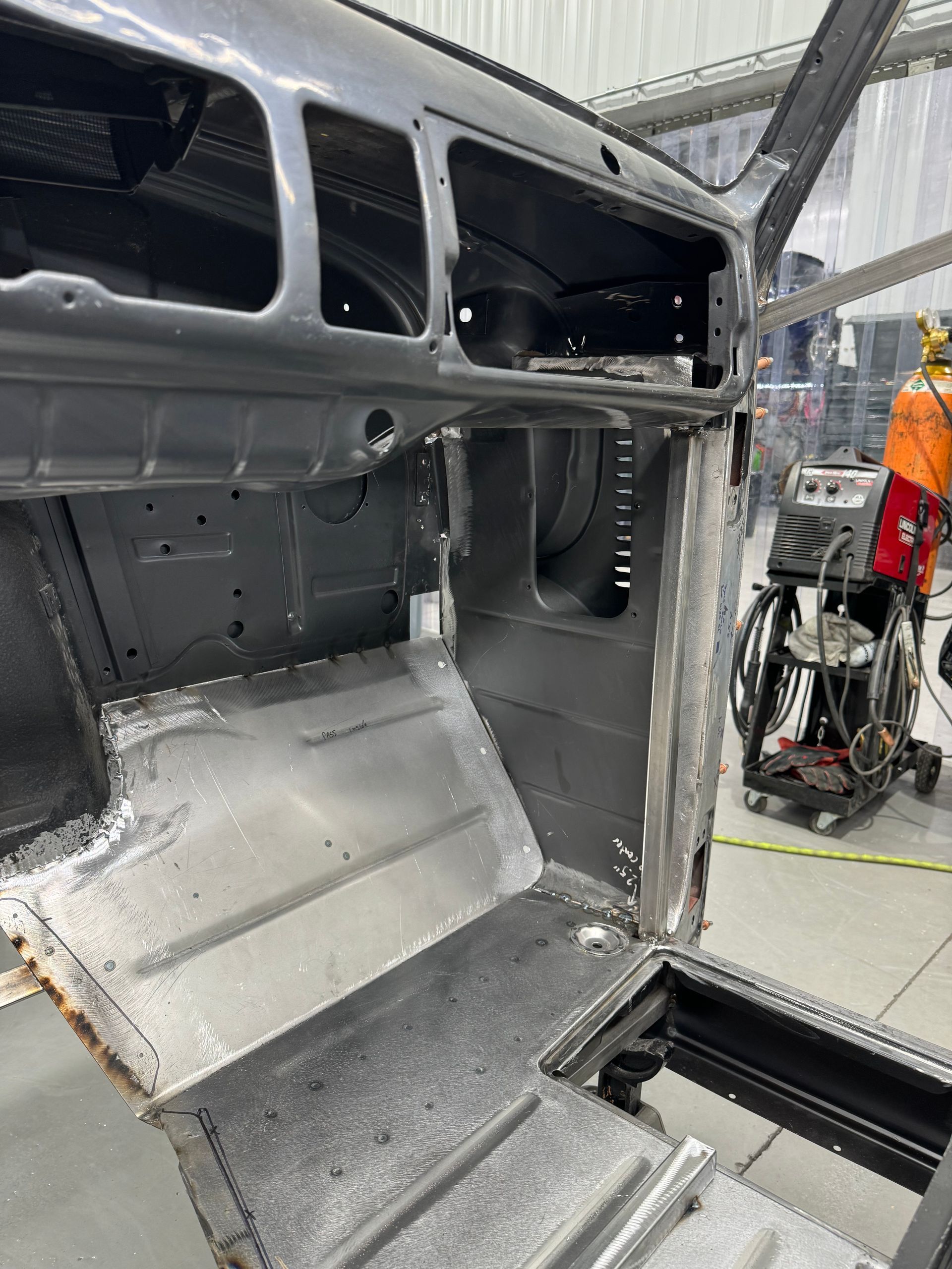 Bare metal car interior under repair, with exposed panels and a worker in the background