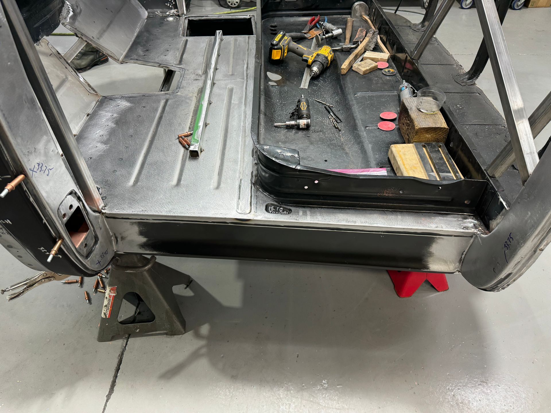 Disassembled vehicle interior with exposed metal framing, tools, and parts on a workshop floor.