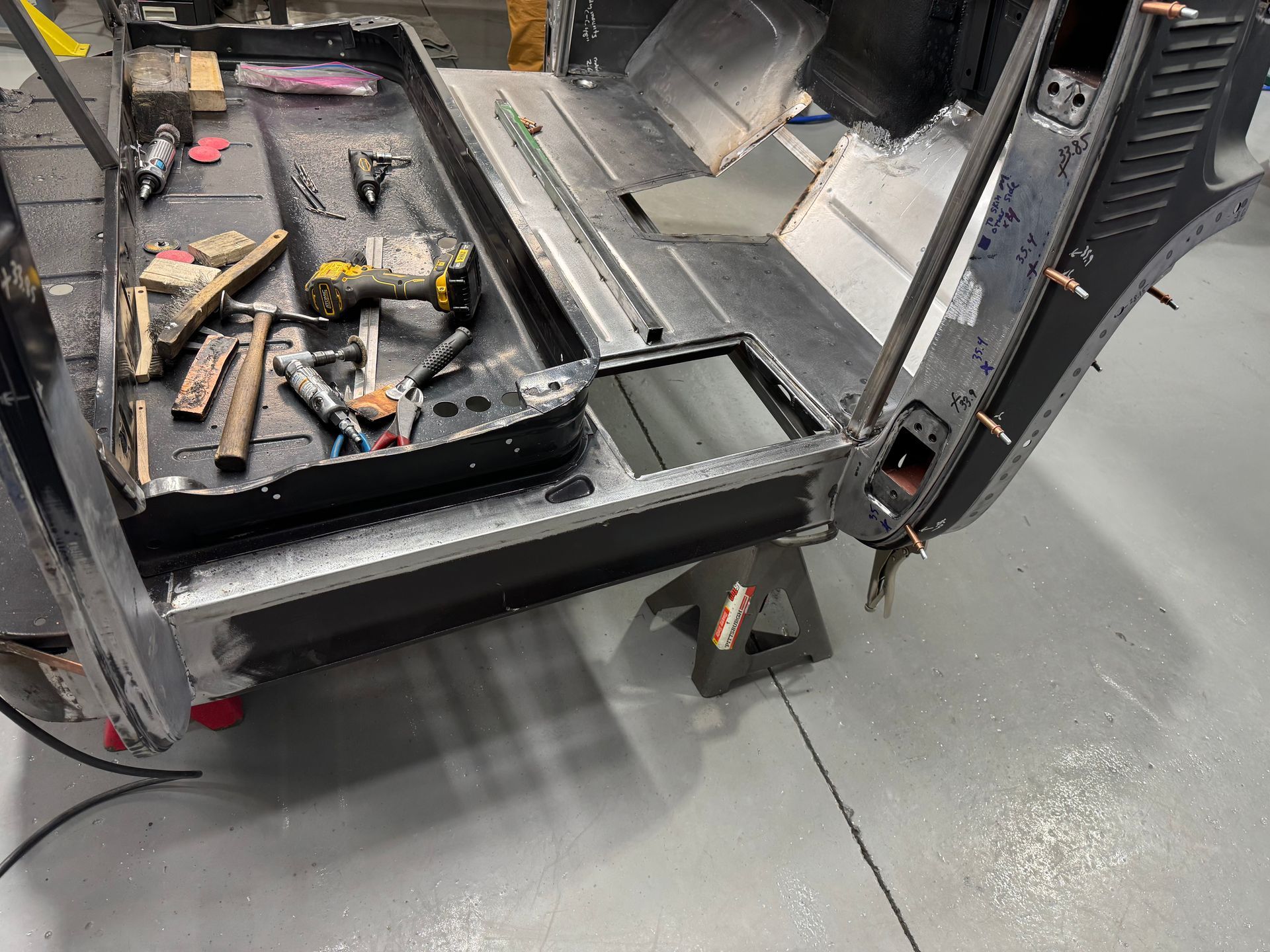 Damaged black forklift with broken frame and scattered tools on a wet concrete floor in a workshop
