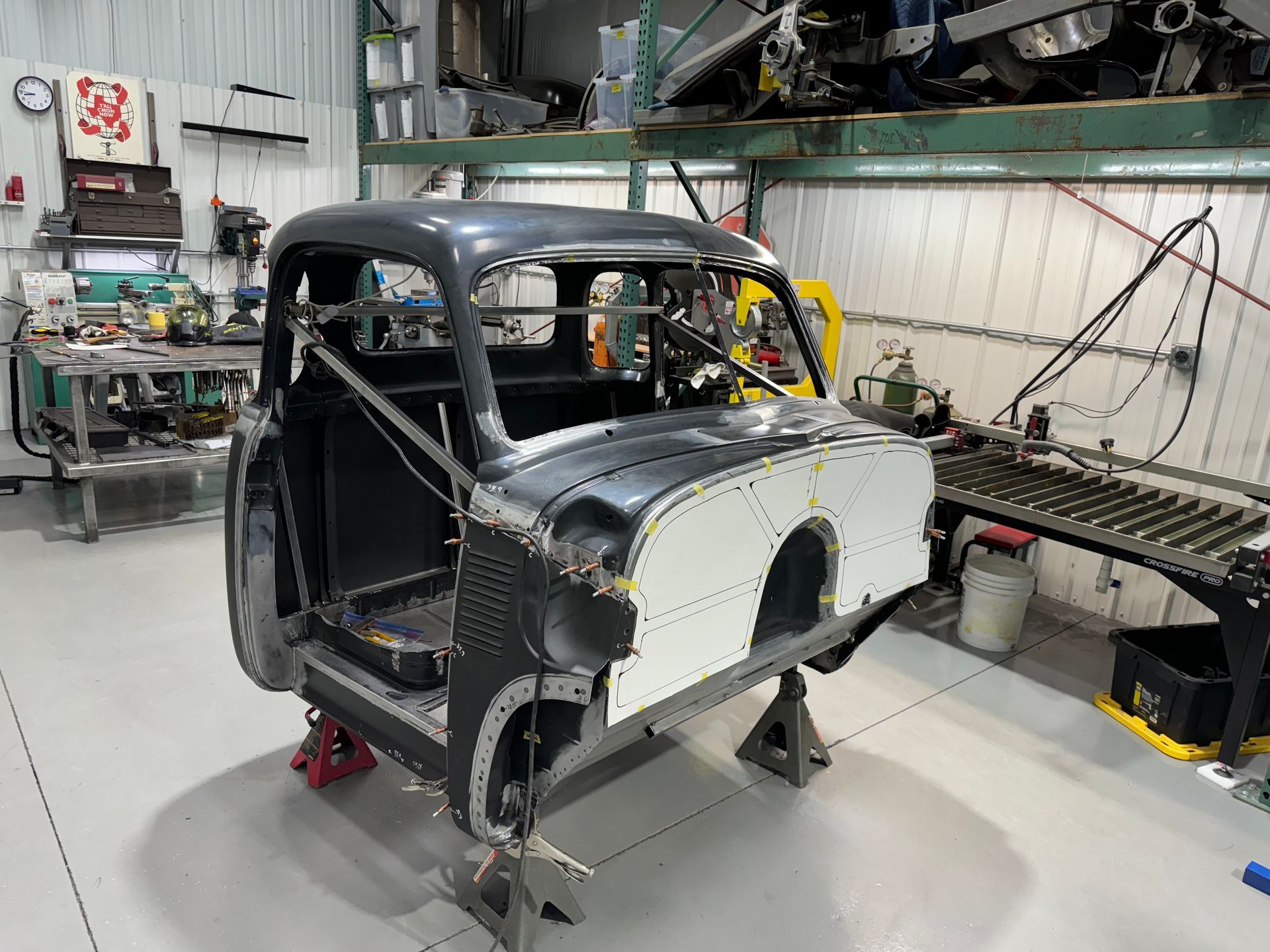 Partially assembled classic car body in a workshop with exposed metal panels and tools nearby