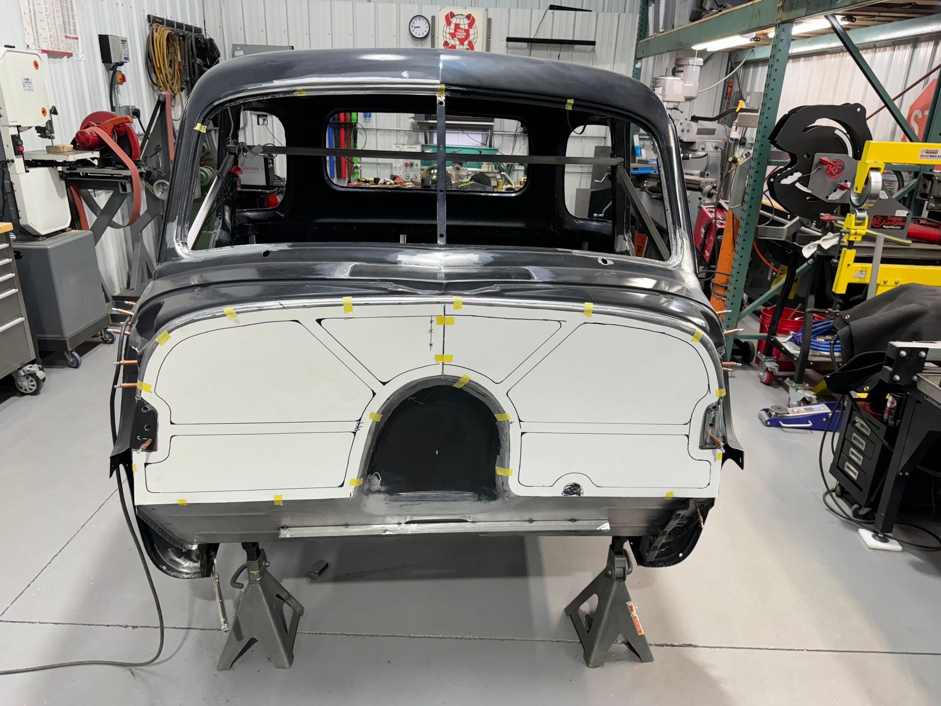Classic car body in a workshop, stripped and under repair on stands, with tools and equipment around it
