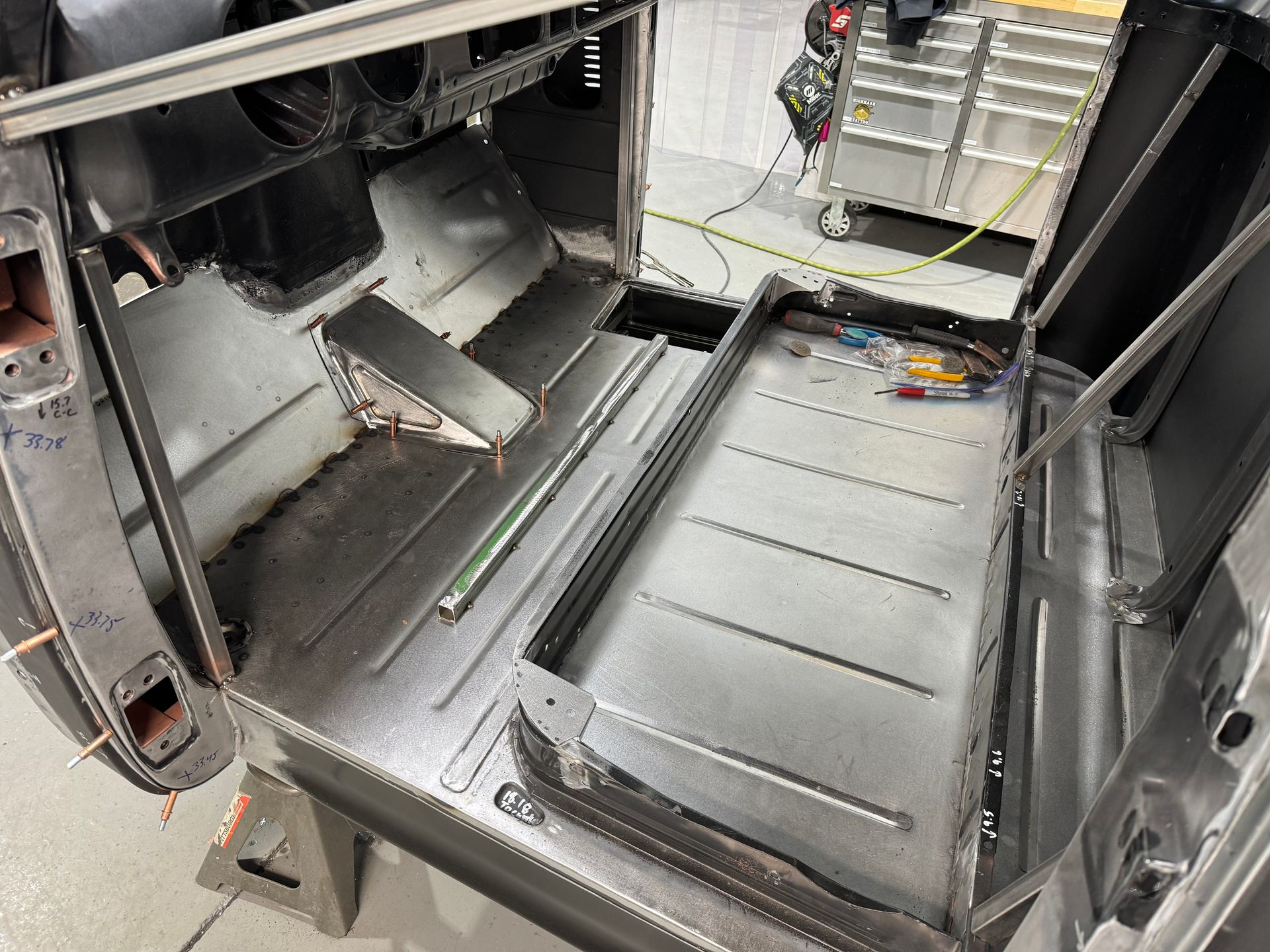 Open vehicle floor with exposed metal panels, storage compartments, and wiring during maintenance