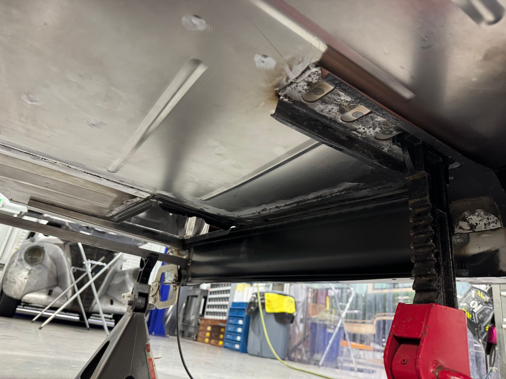 Under-vehicle view of a machine with a black belt and red motor assembly in a workshop