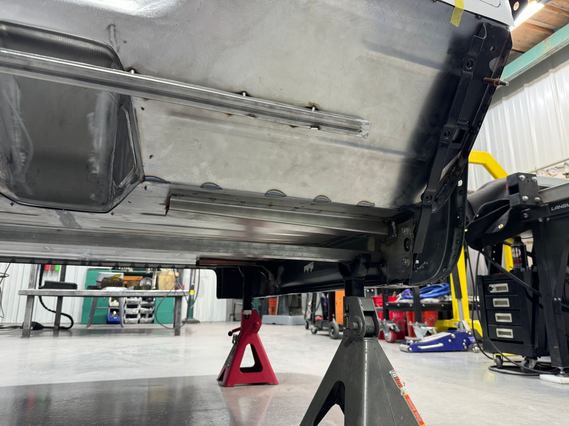 Underside of a car raised on jack stands in a mechanic’s shop, with tools and equipment nearby