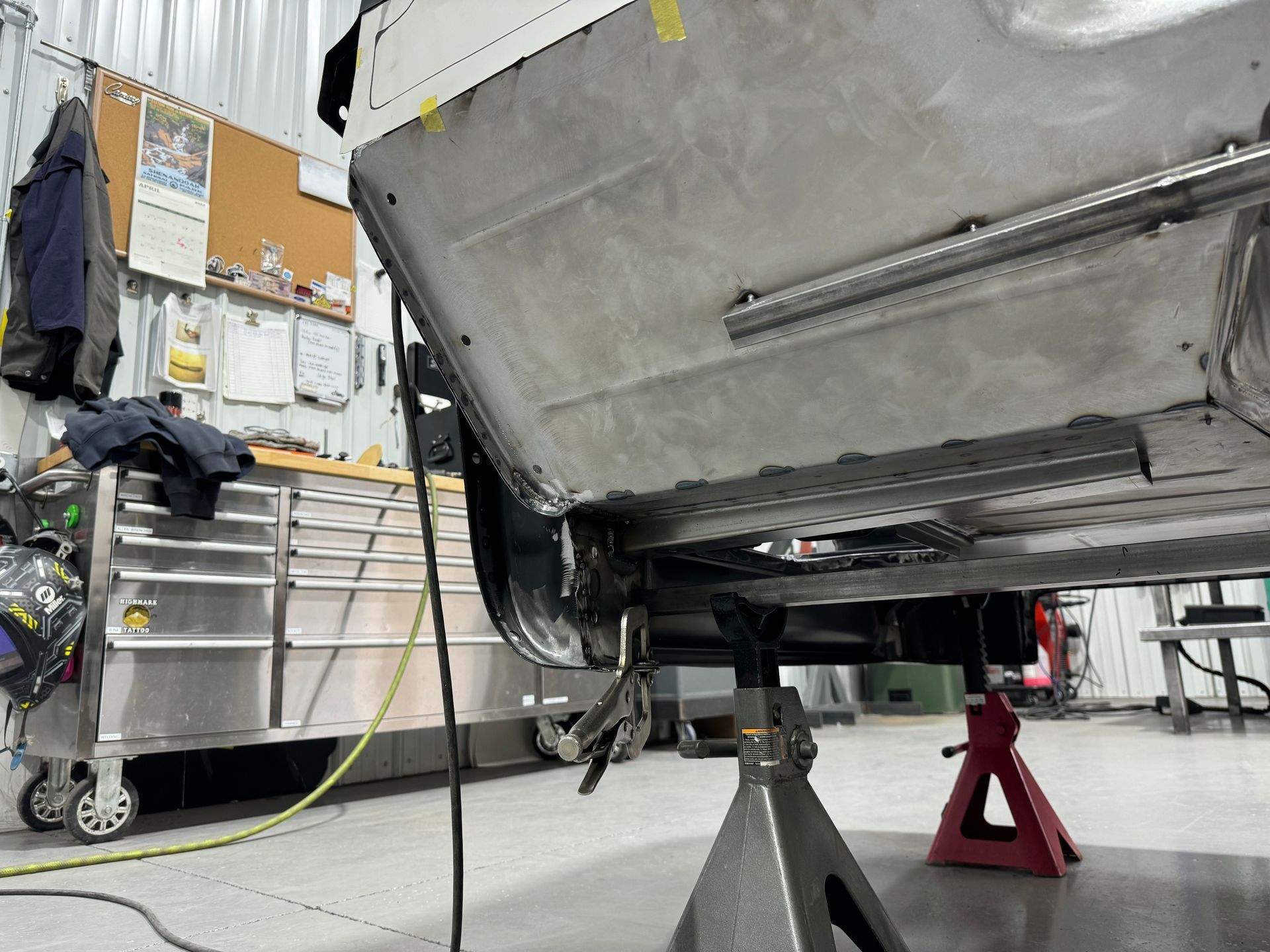 Undercarriage of a car on stands in a garage, with tools and shelves in the background
