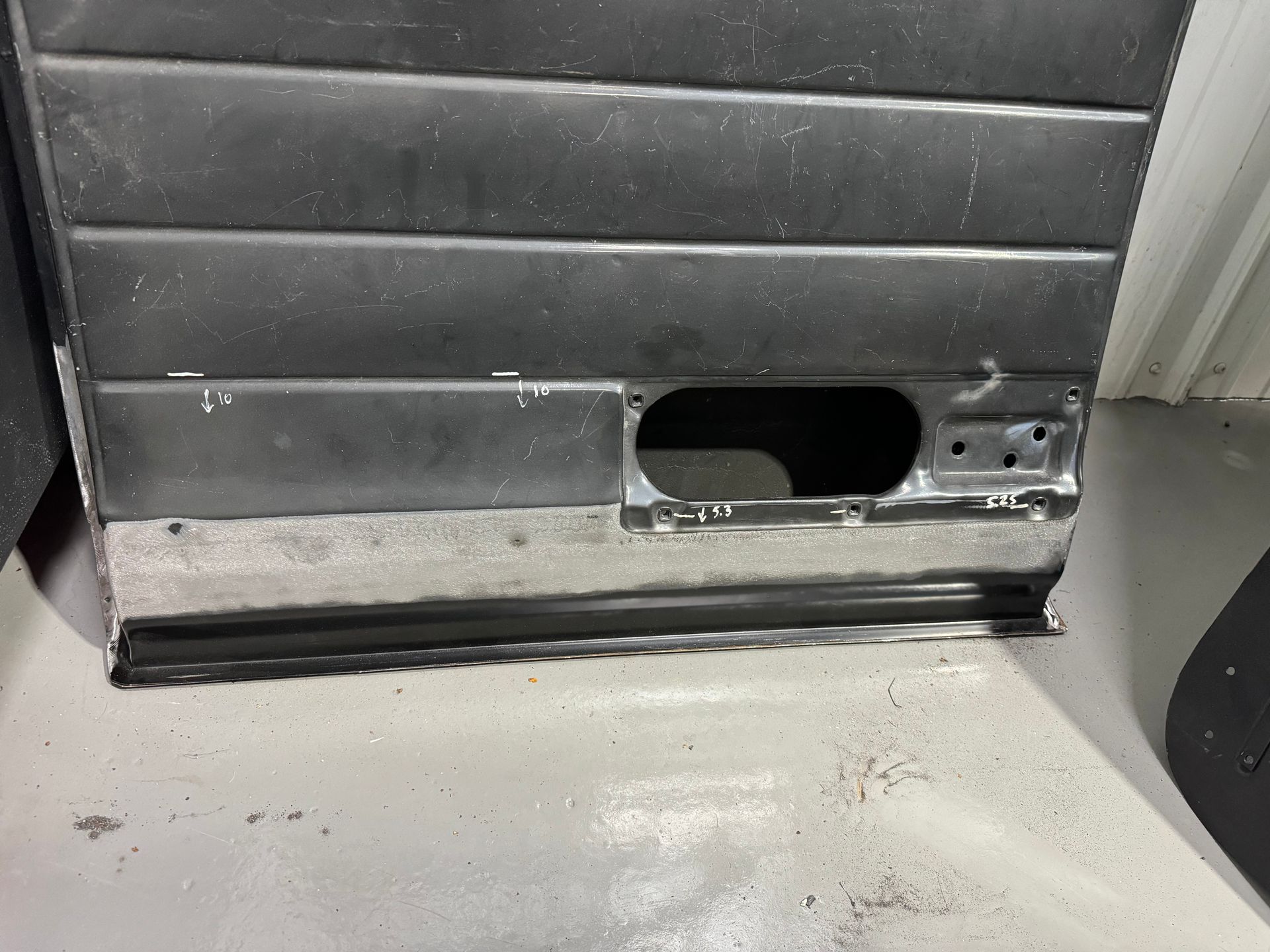Close-up of a gray metal panel with a black oval opening near the bottom and some scuffs on the floor.