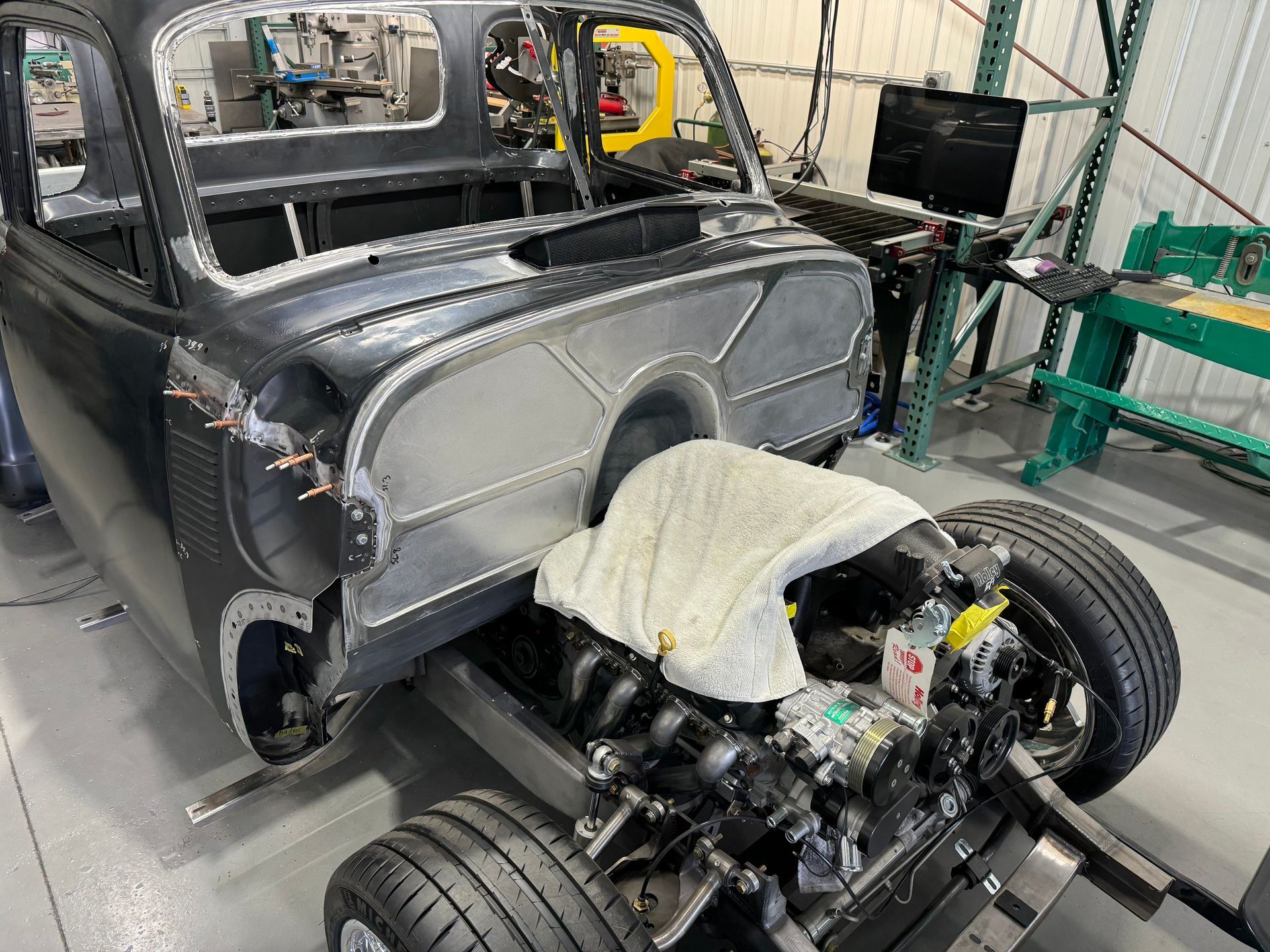 Classic car body under restoration with exposed front suspension and a shop towel covering the engine bay