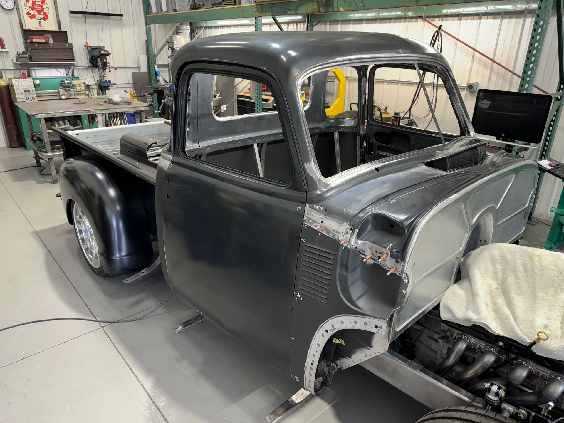 Gray vintage pickup truck cab in a workshop, mid-restoration with exposed body panels and engine bay