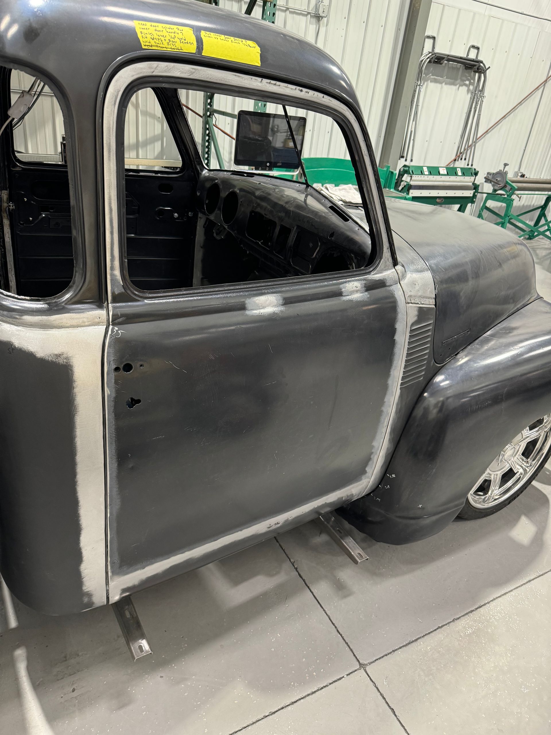 Classic black car body in a workshop, partially restored with bare metal patches and open door frame.