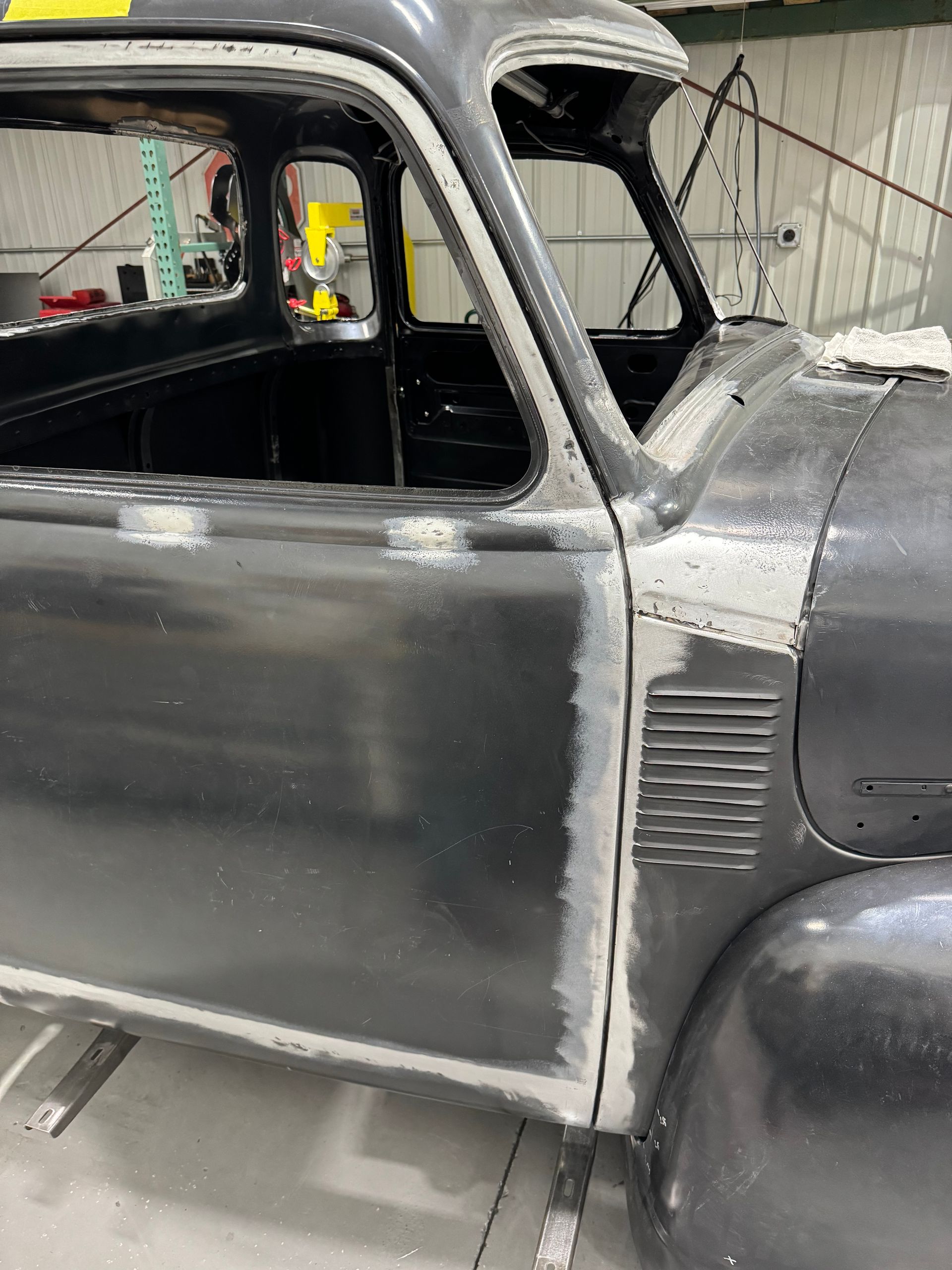 Gray vintage car body in a workshop, viewed from the side with hood and door area visible
