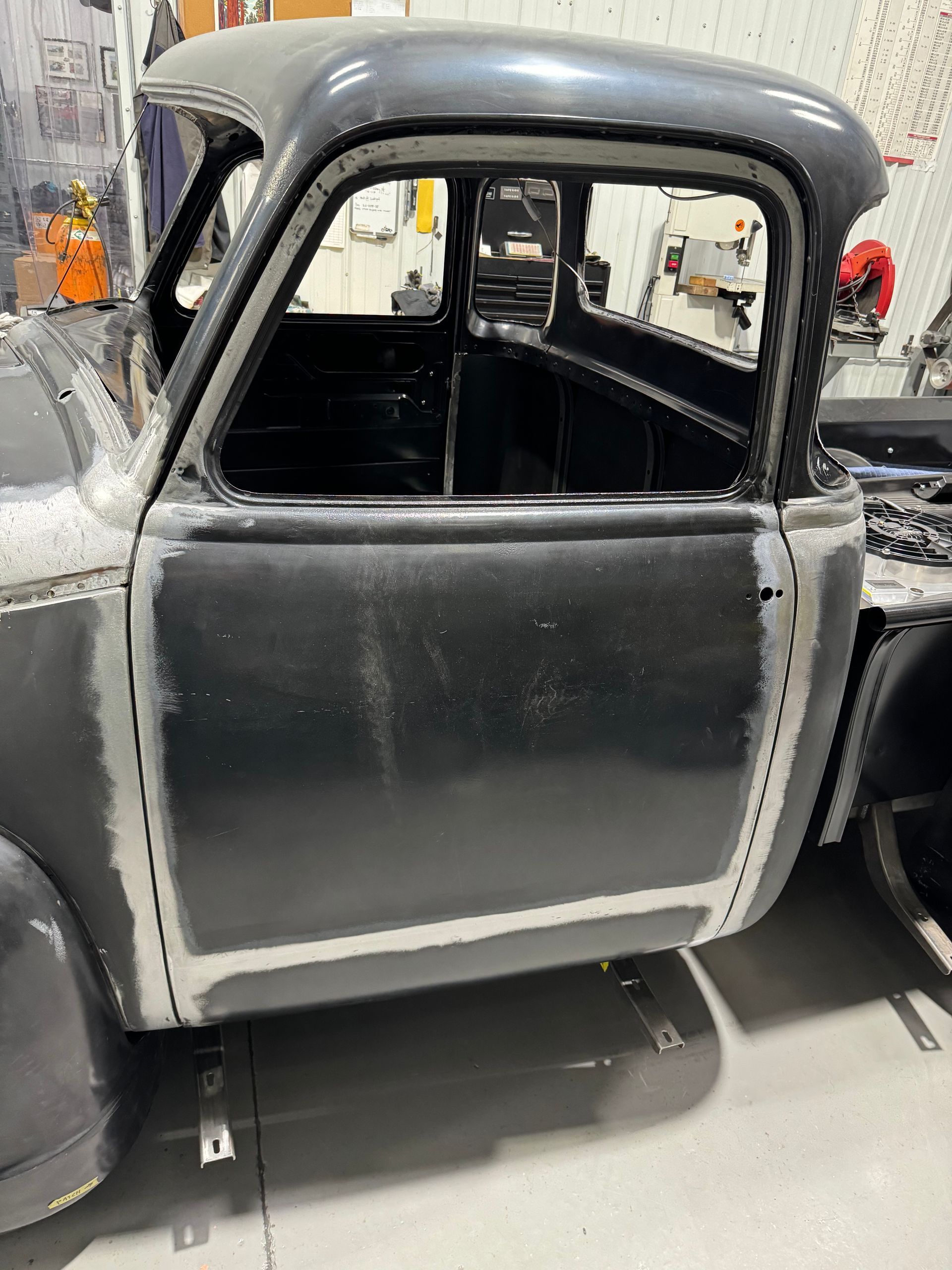 Black vintage car body in a workshop, with primed gray panels and exposed interior.