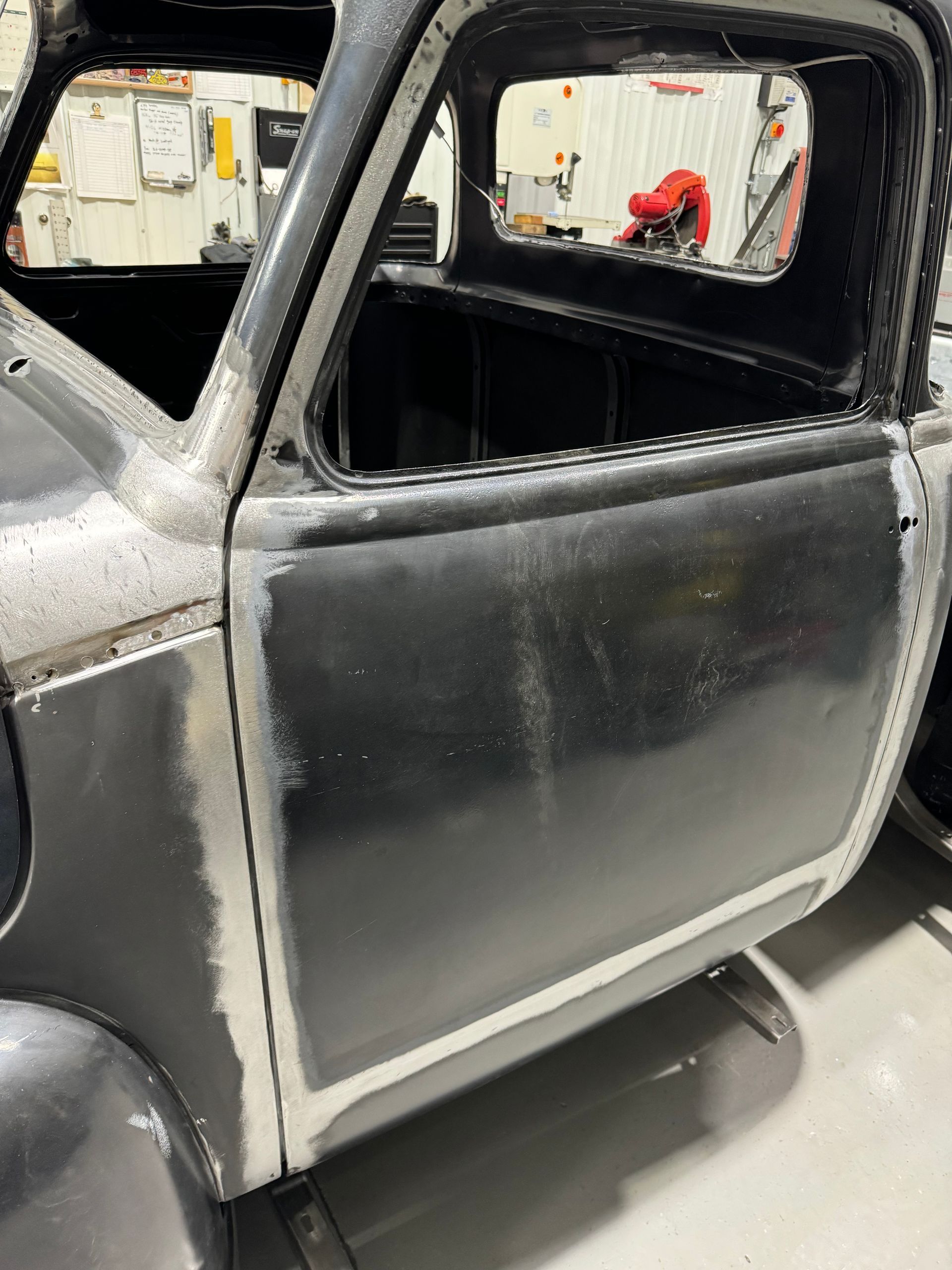 Black classic car door and window opening in a workshop, showing primed bodywork and unfinished trim