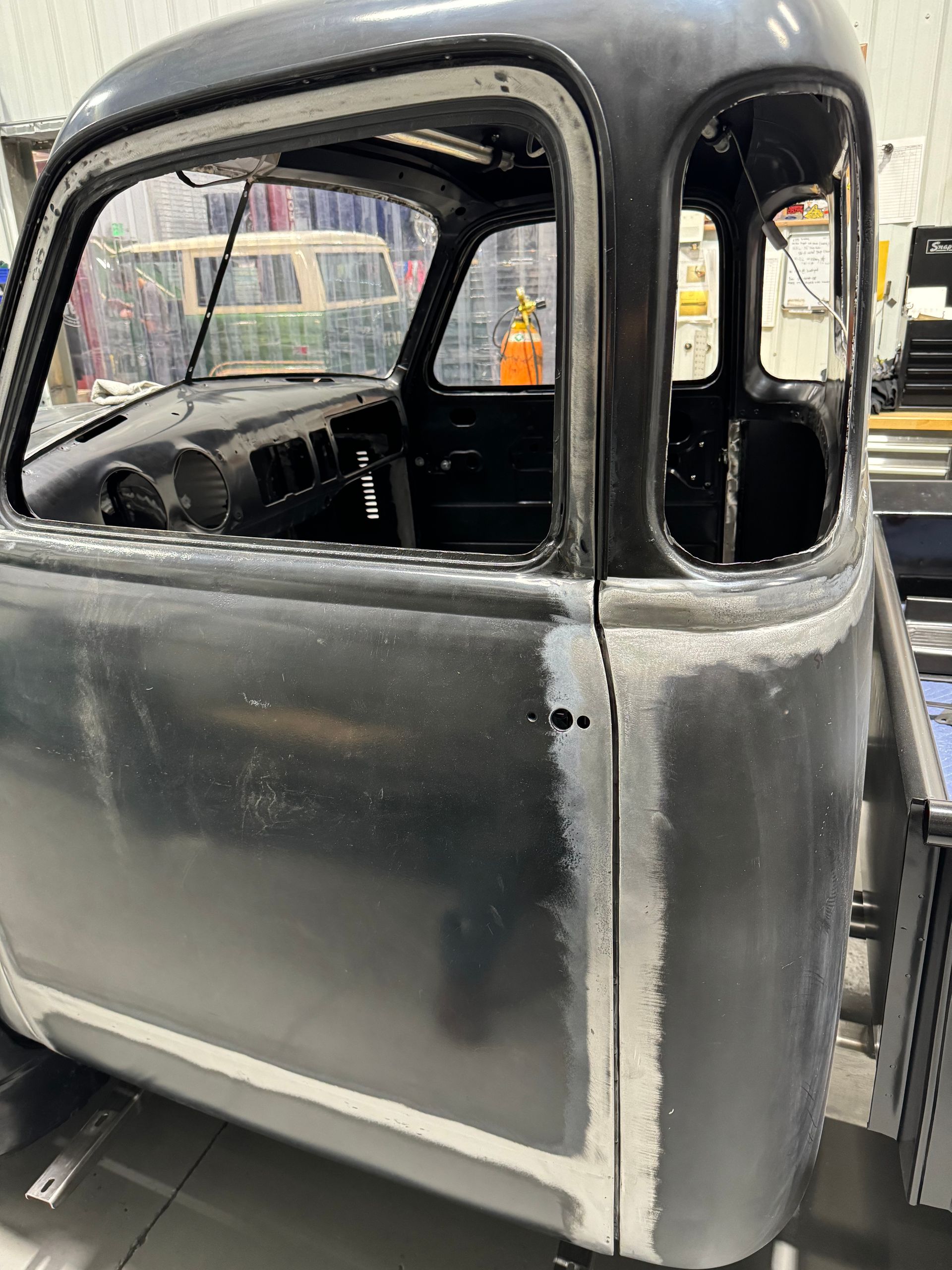 Black vintage car body in a workshop, showing the side windows and door panel during restoration