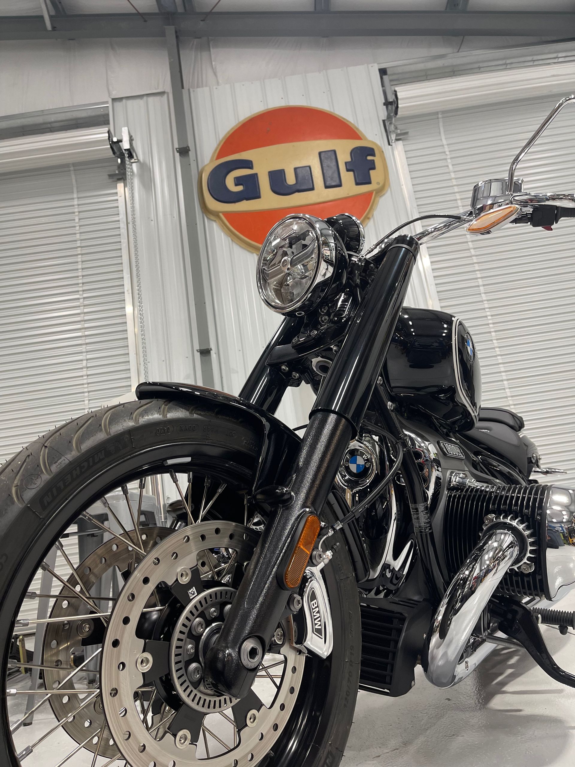 Black custom motorcycle with chrome details parked indoors beneath a Gulf sign.