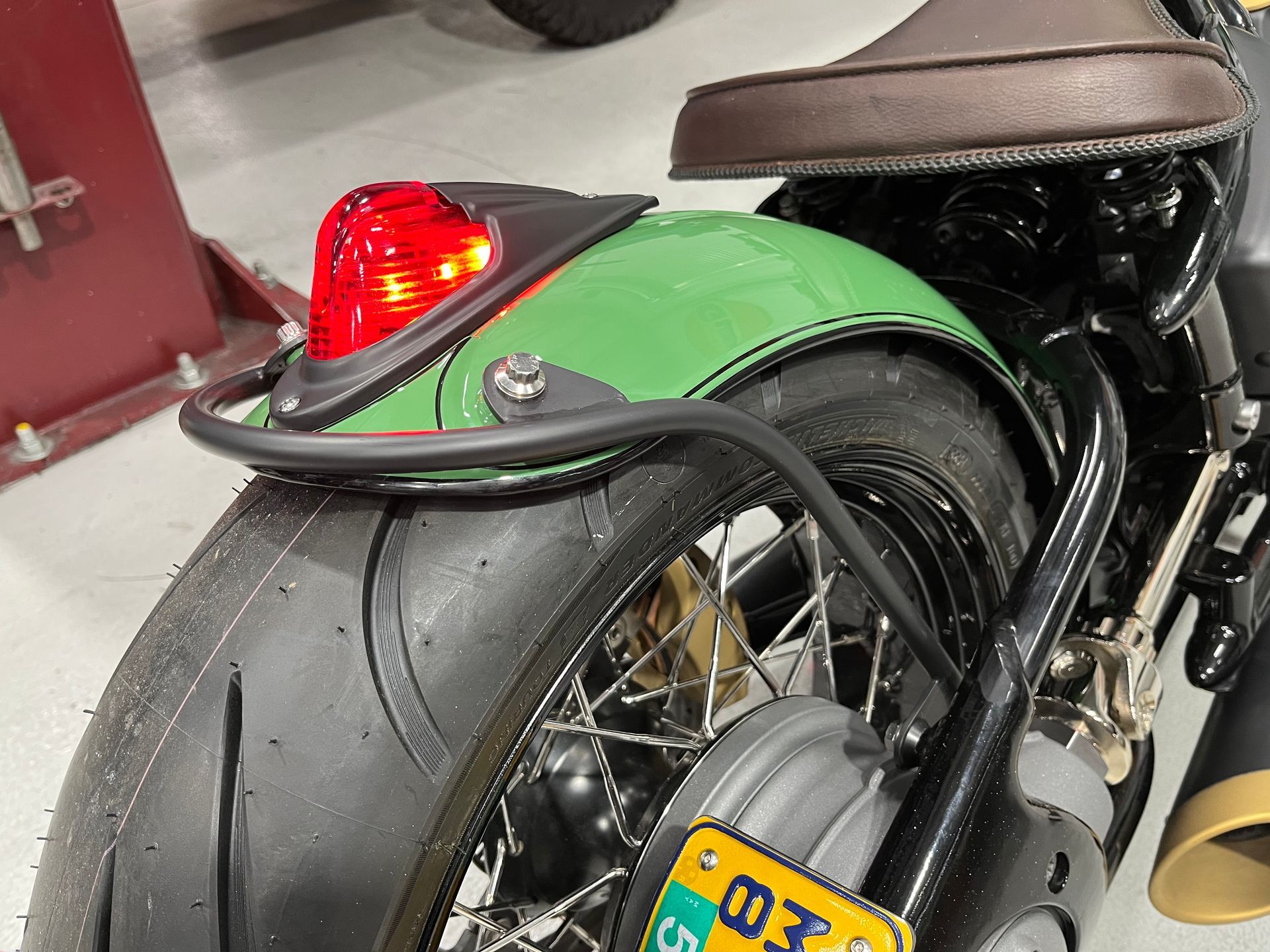 Close-up of a custom motorcycle rear wheel with green fender, red tail light, and yellow license plate