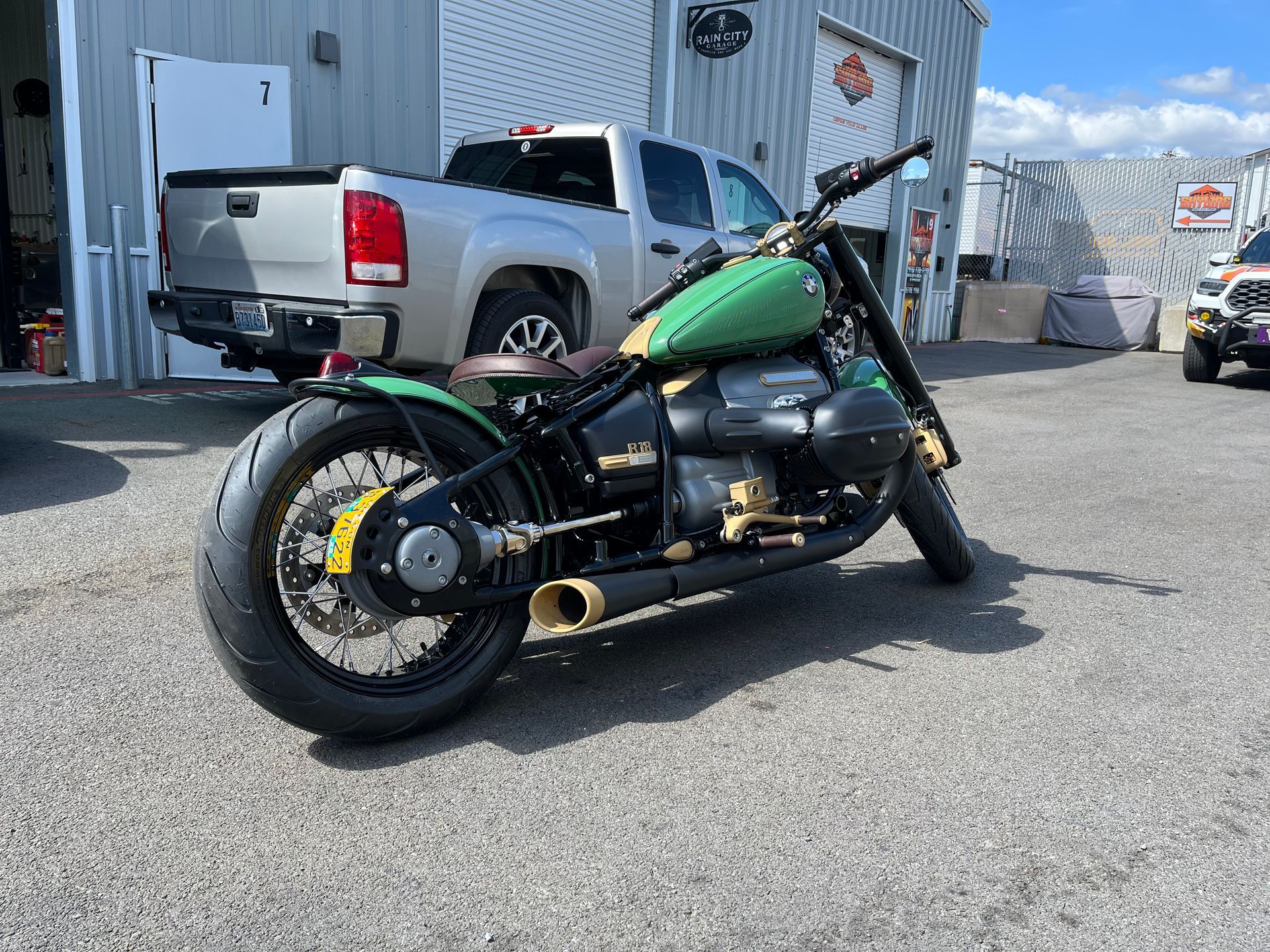 Green and black custom motorcycle parked beside a white pickup truck in an industrial lot