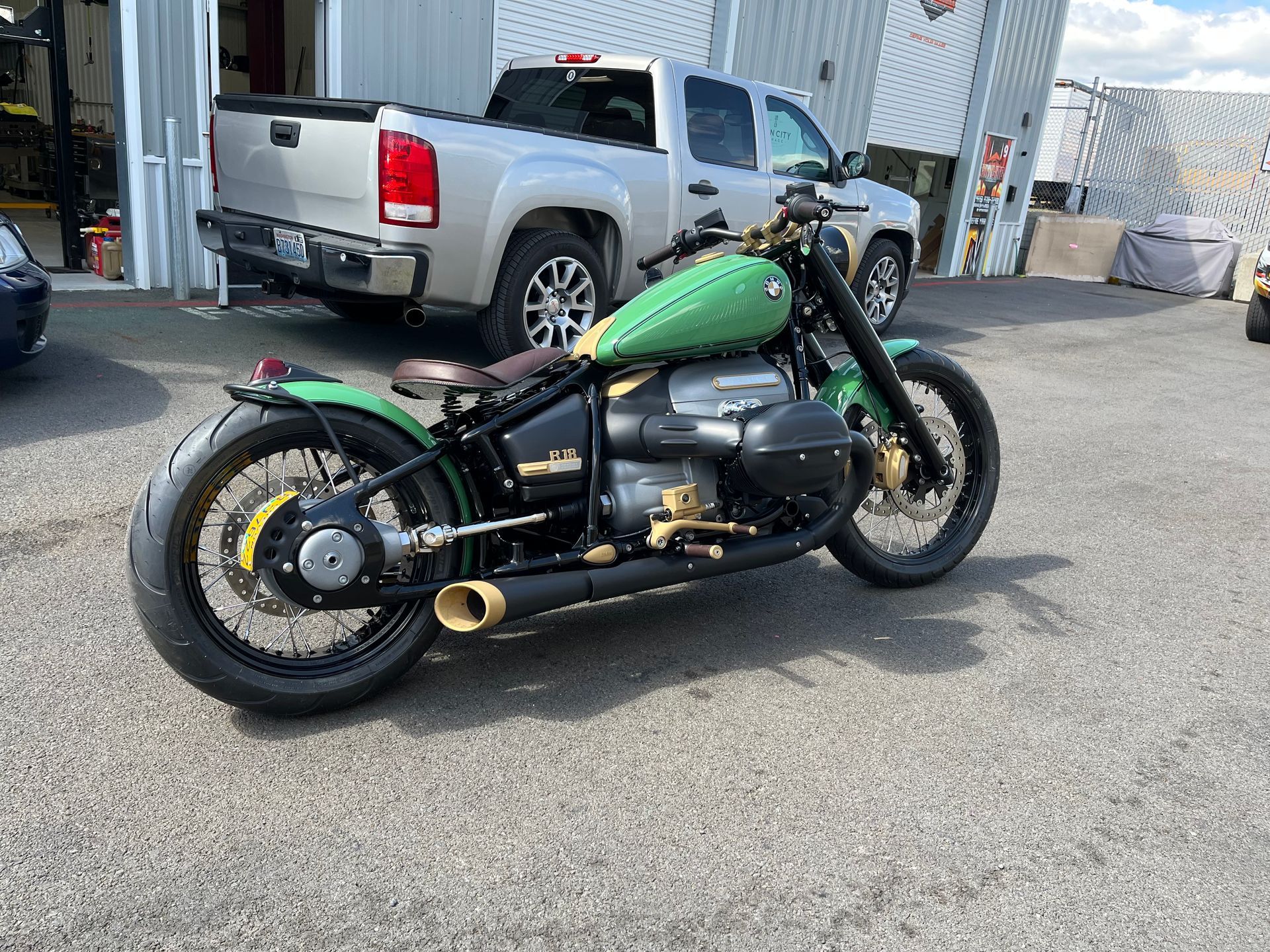 Green custom motorcycle parked outside an industrial building, with a silver pickup truck in the background