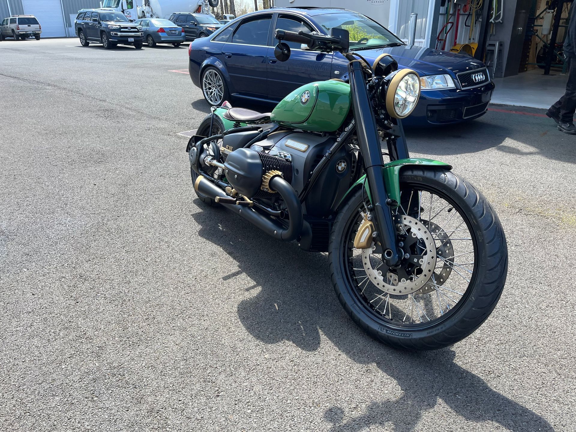 Green vintage motorcycle parked on a street, with cars in the background.