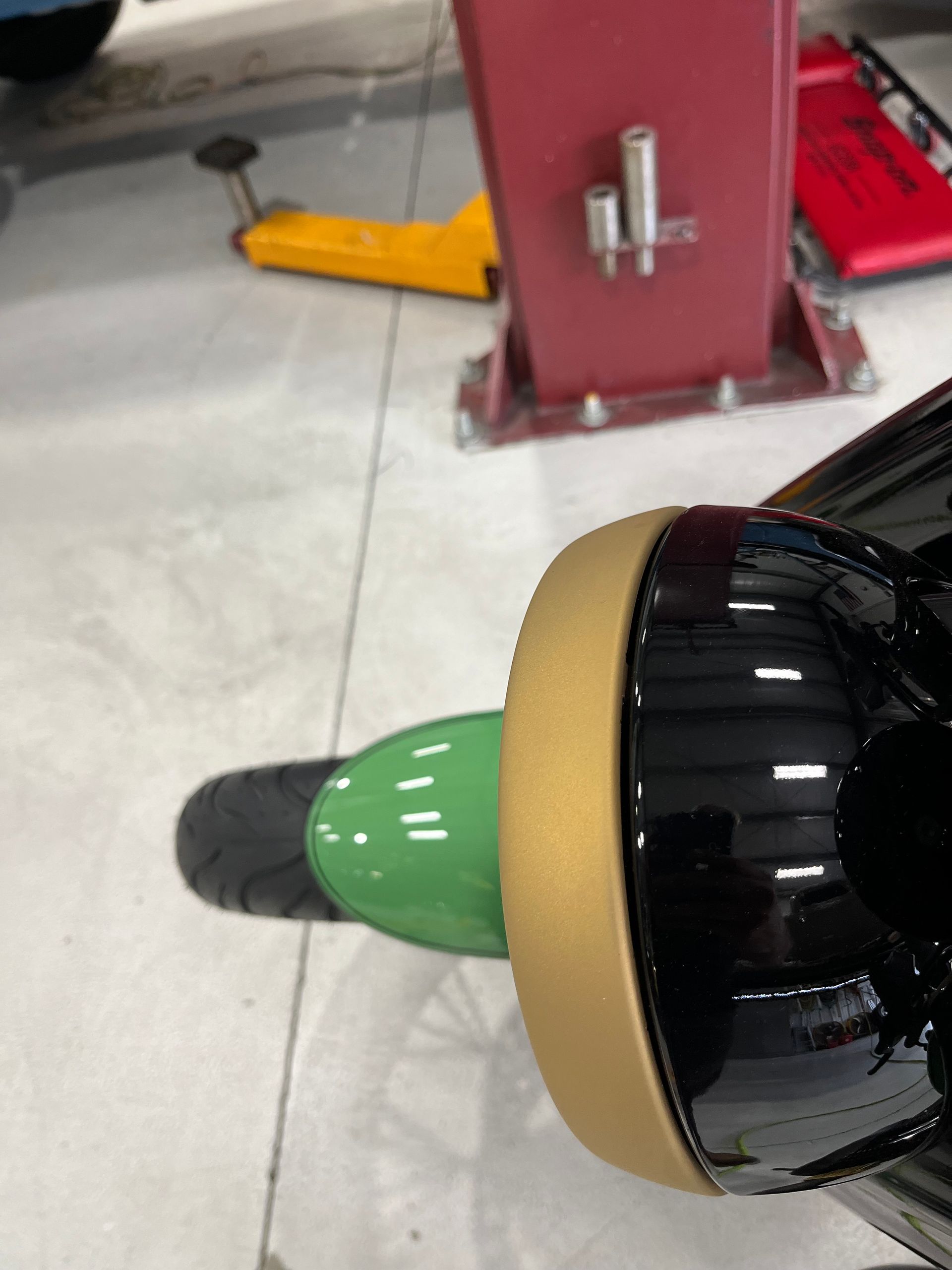 Close-up of a black, green, and tan object on a workshop floor near a red machine base