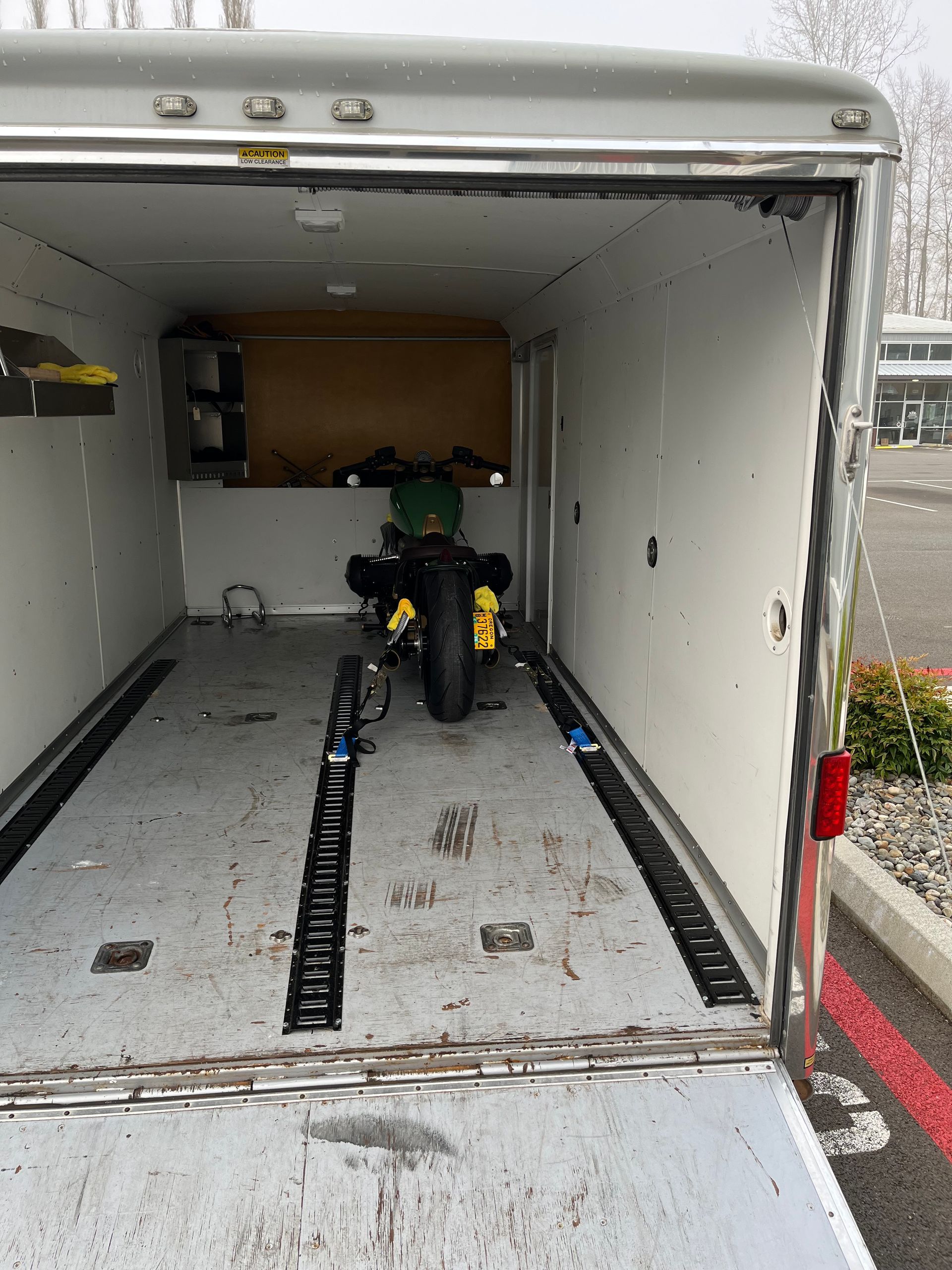 Motorcycle strapped inside an open cargo trailer, viewed from the rear at a parking lot.