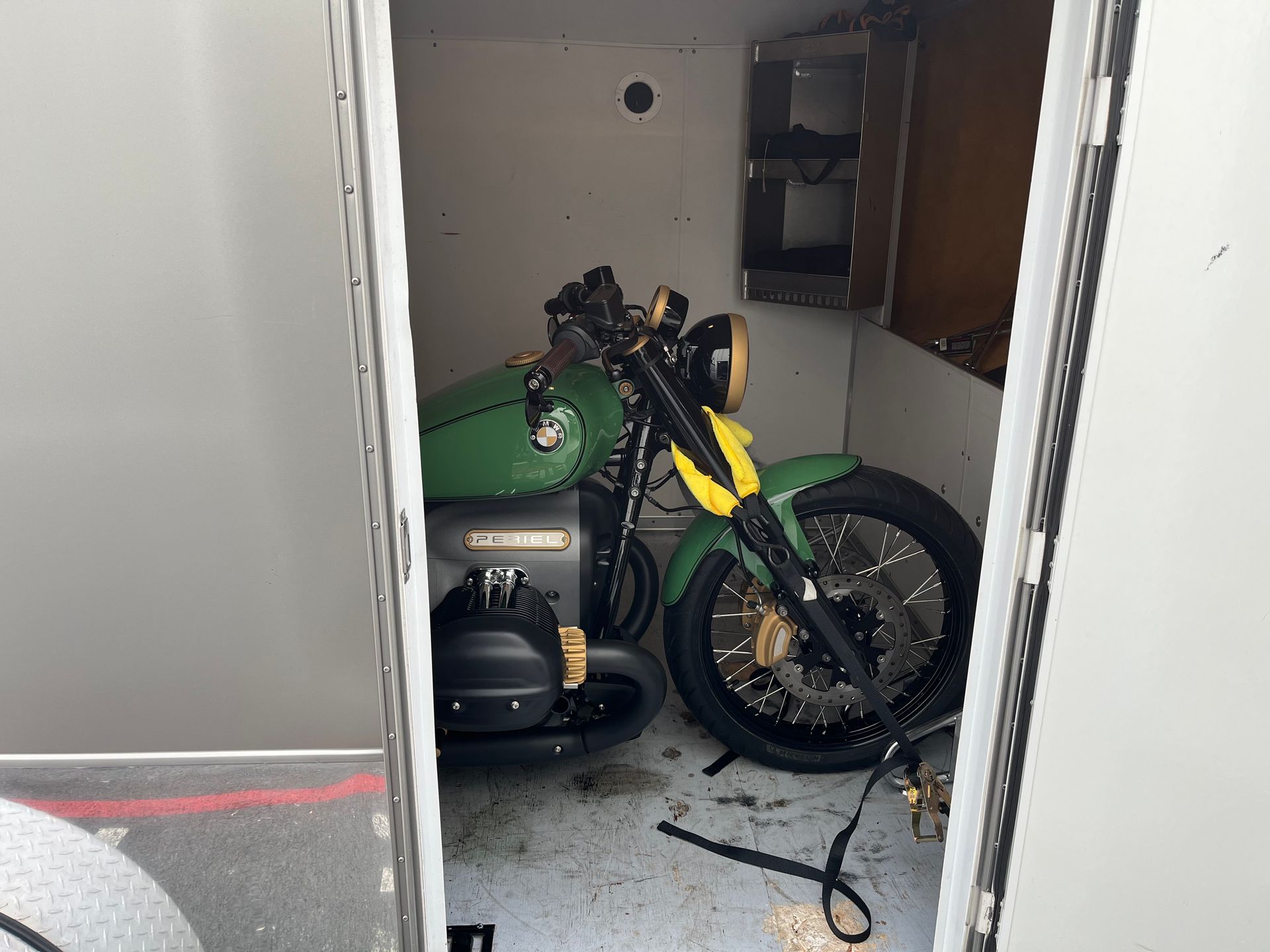 Motorcycle parked in a small garage or storage room with a green item beside it and scattered cables on the floor