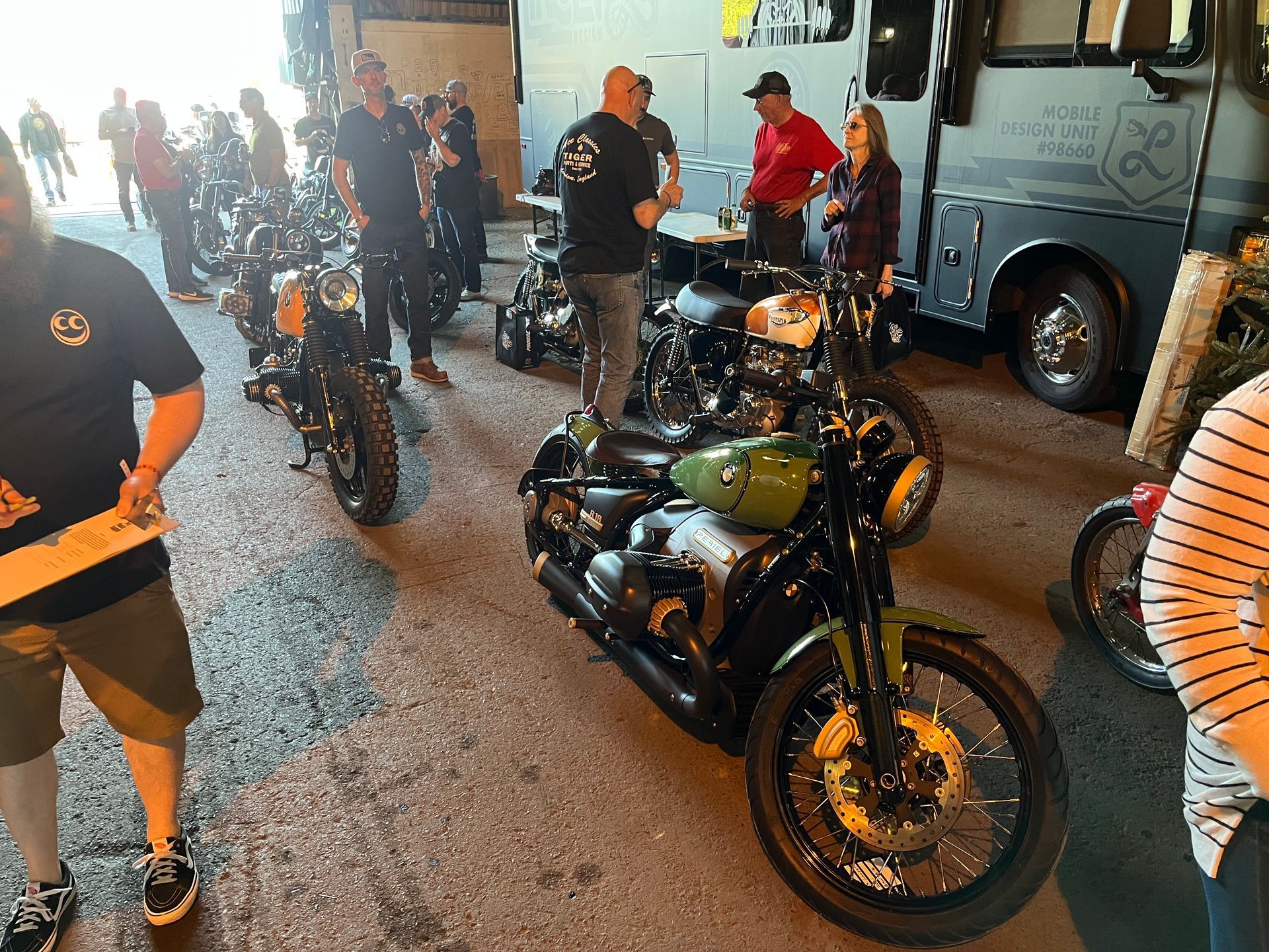 Motorcycles and riders gathered inside a garage-like space, with a black-and-gold bike in the foreground.
