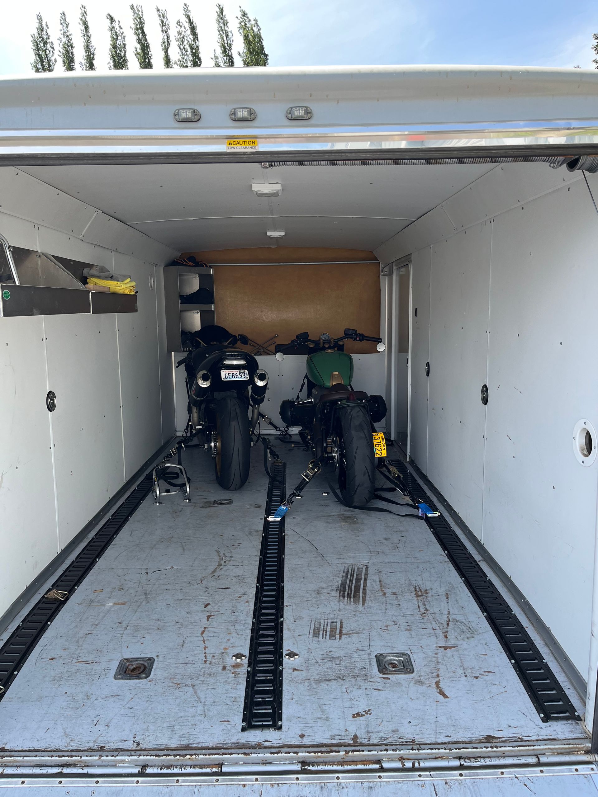 Inside an empty cargo trailer, two motorcycles are parked on the floor.