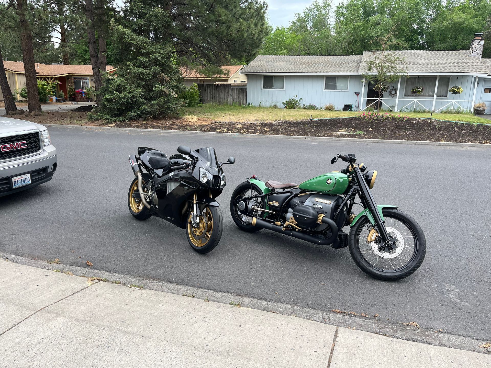 Two parked motorcycles on a residential street, one black and one green, beside a driveway.