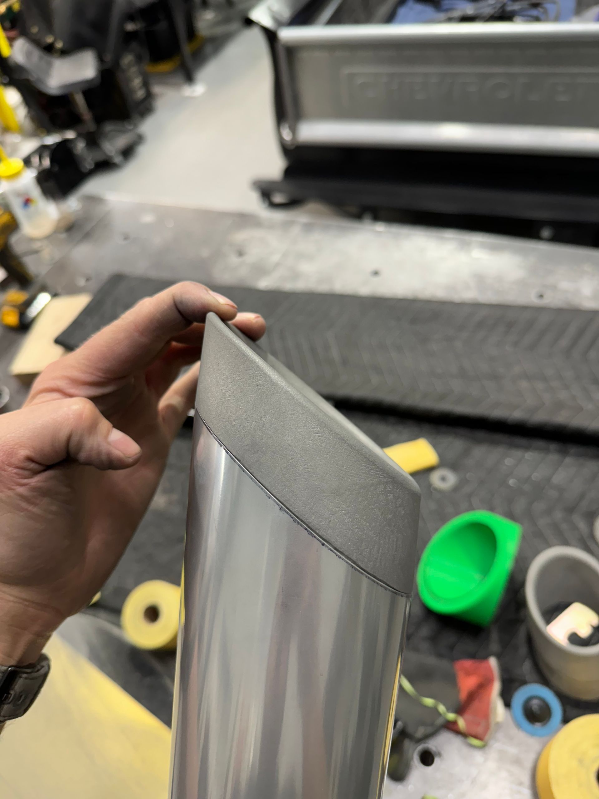 Hand holding a gray textured foam strip over a workbench with tools and materials scattered around