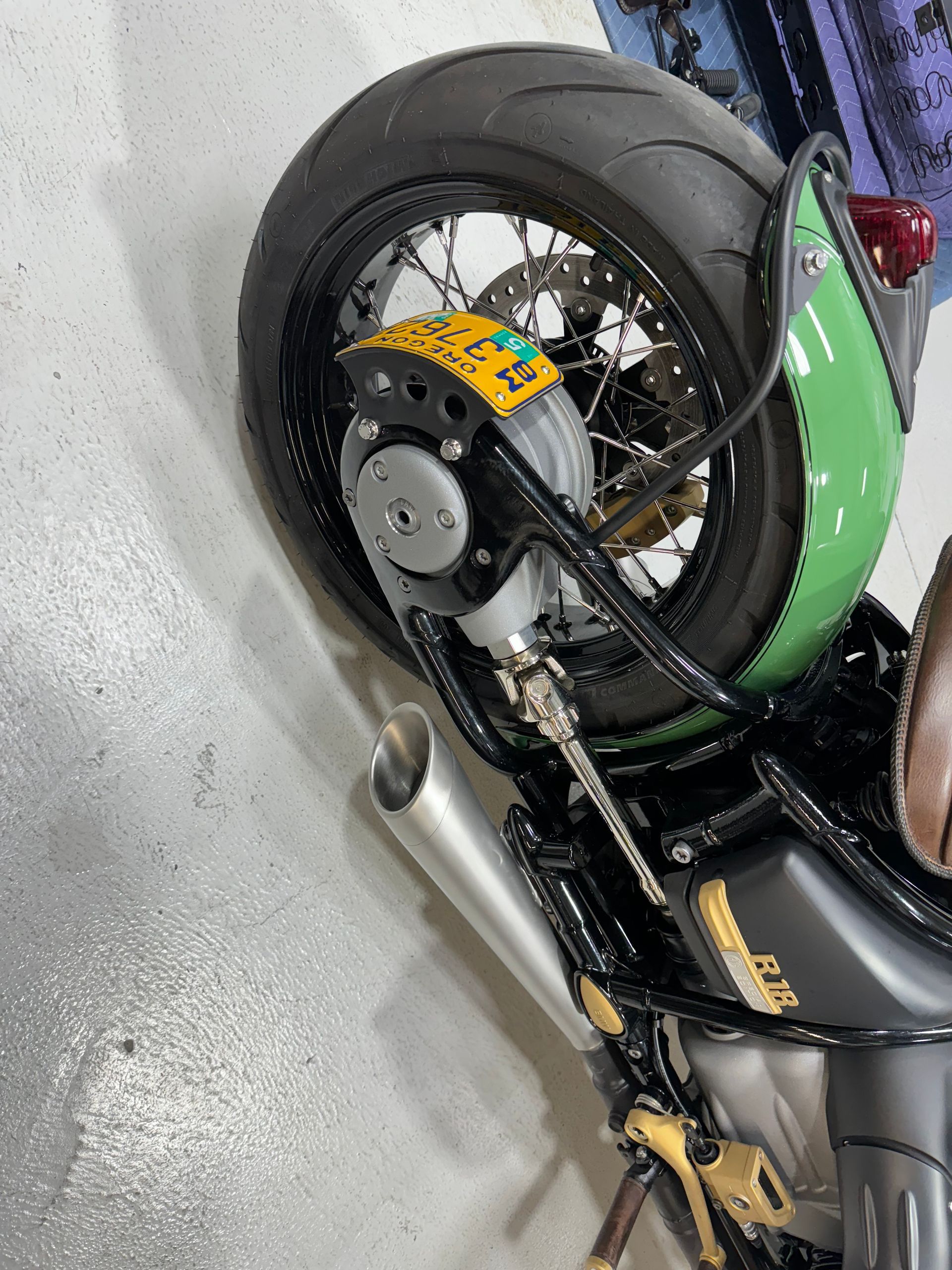 Black and green sport motorcycle parked indoors, side view showing rear wheel and exhaust.