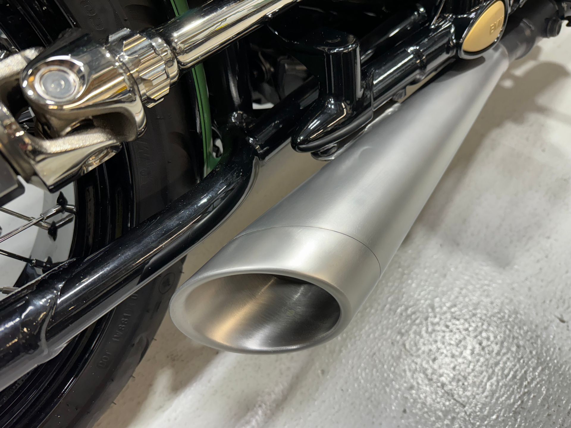 Close-up of a motorcycle’s chrome exhaust pipe and black frame on a light floor.