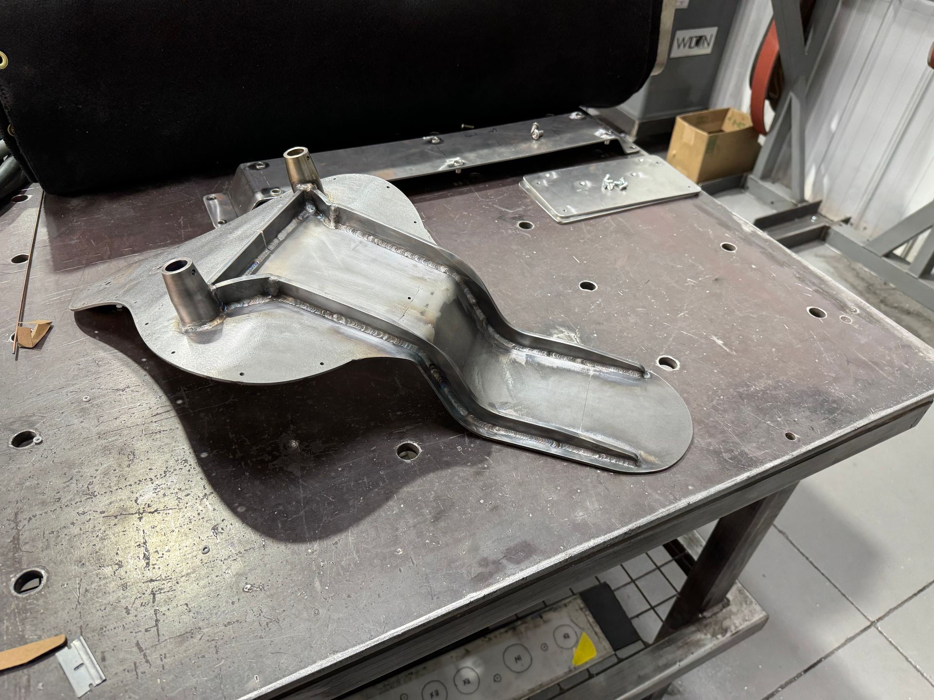 Metal wheel clamp on a workbench in a workshop, with a curved gray base and a black handle.