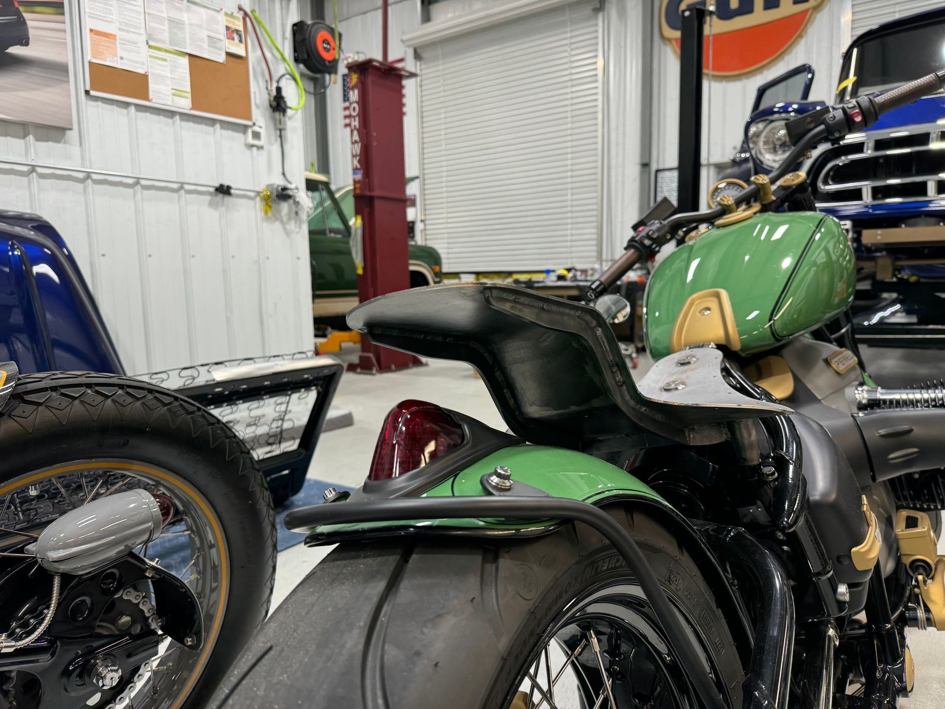 Green motorcycle parked in a garage beside other bikes and equipment