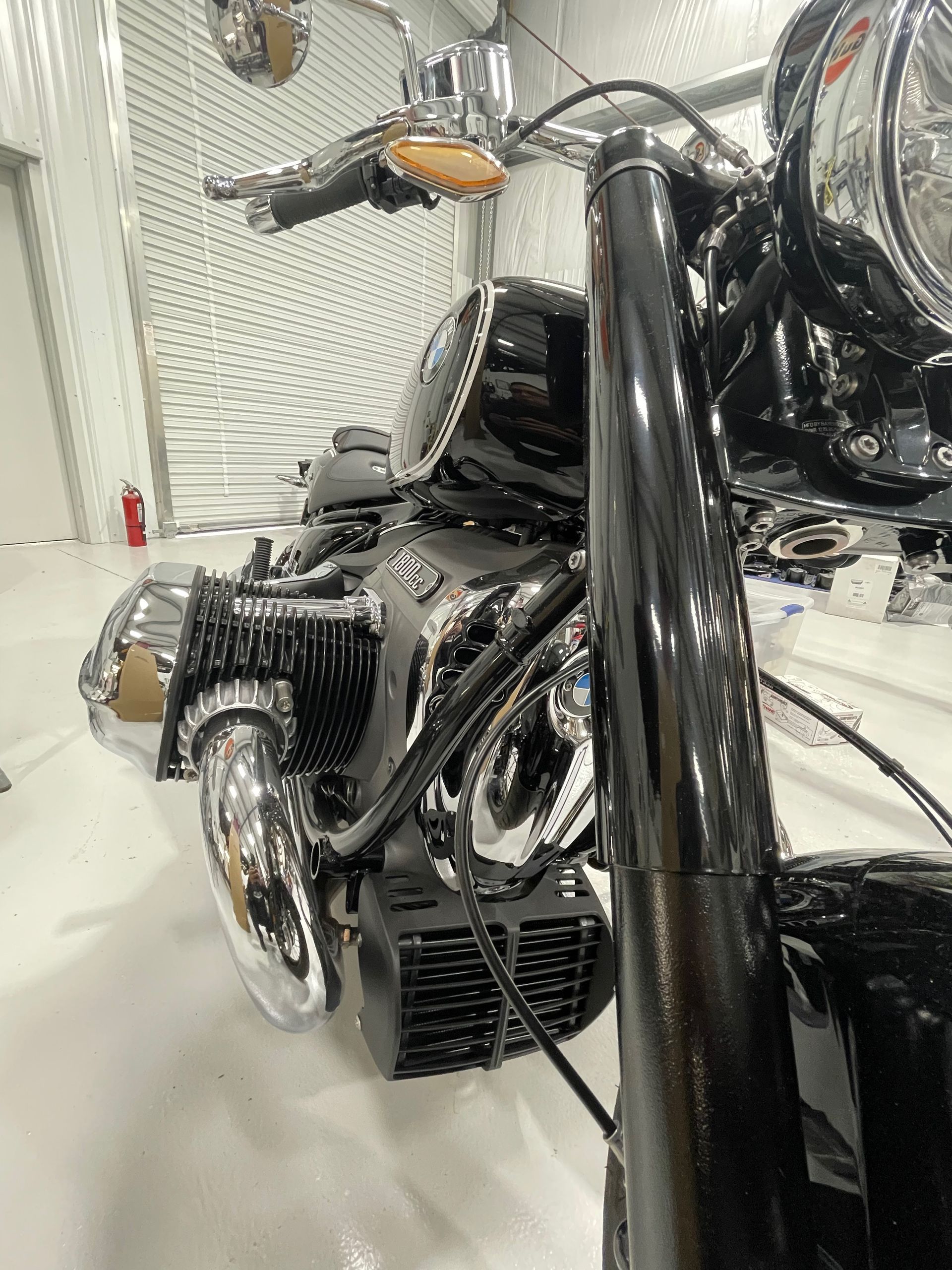 Close-up of a chrome motorcycle engine and front wheel in a white garage workshop.