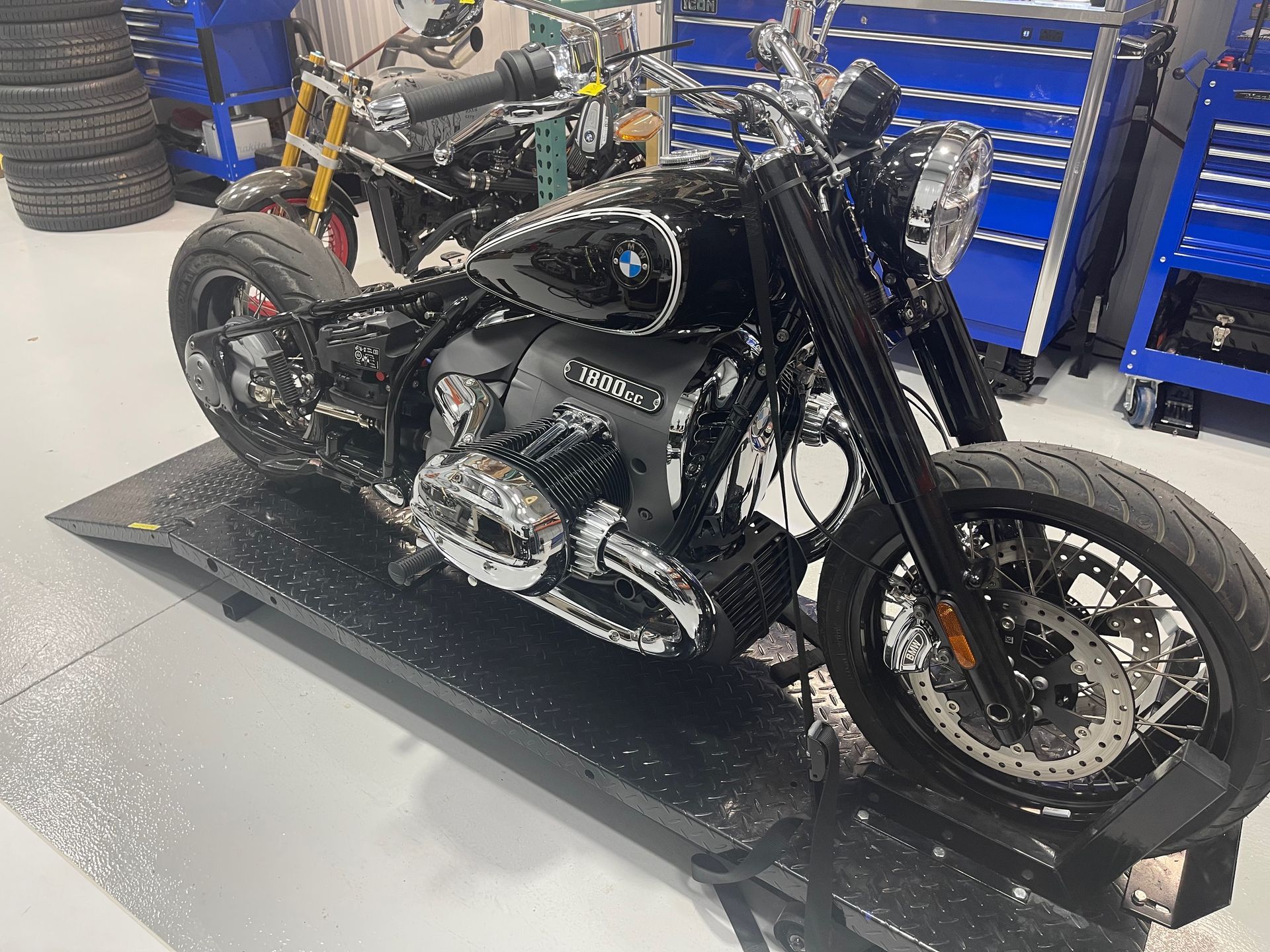 Black custom motorcycle on a shop lift in a garage, with blue tool cabinets in the background