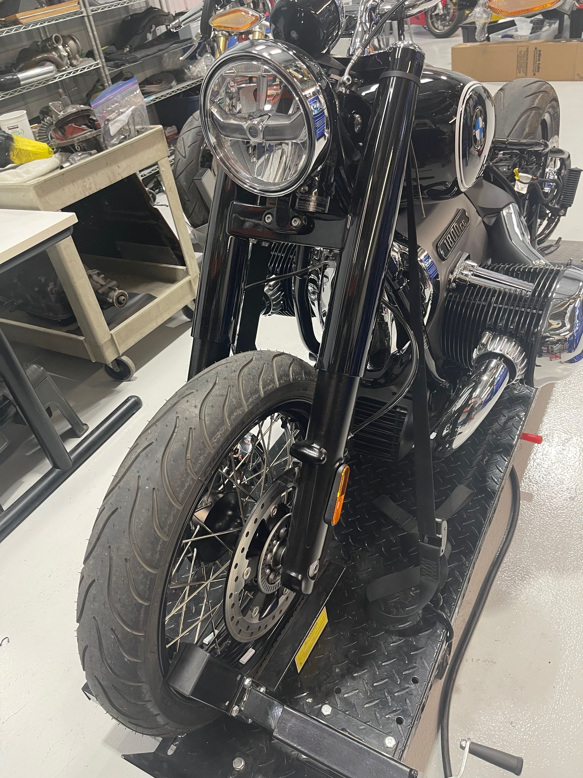 Black motorcycle with a large front wheel in a workshop, viewed from the front-left side.