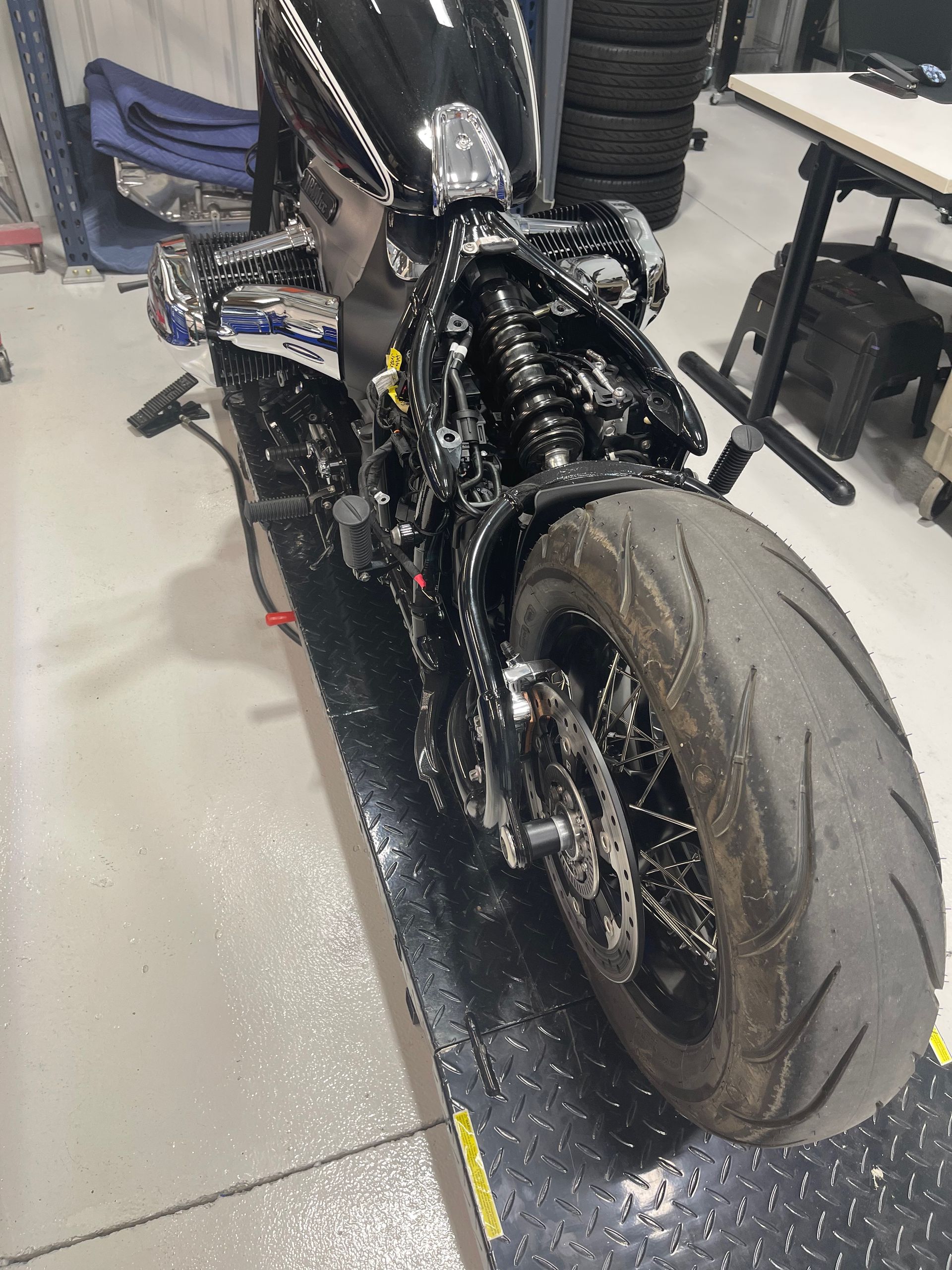 Close-up of a black motorcycle with a wide rear tire in a workshop, covered in a glossy liquid.