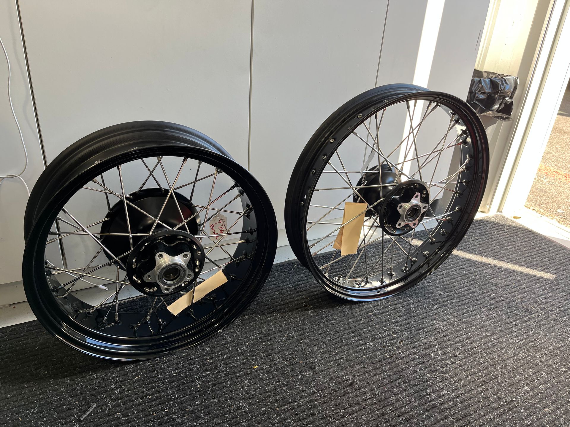 Two black spoked wheels leaning against a wall on a sunlit floor.