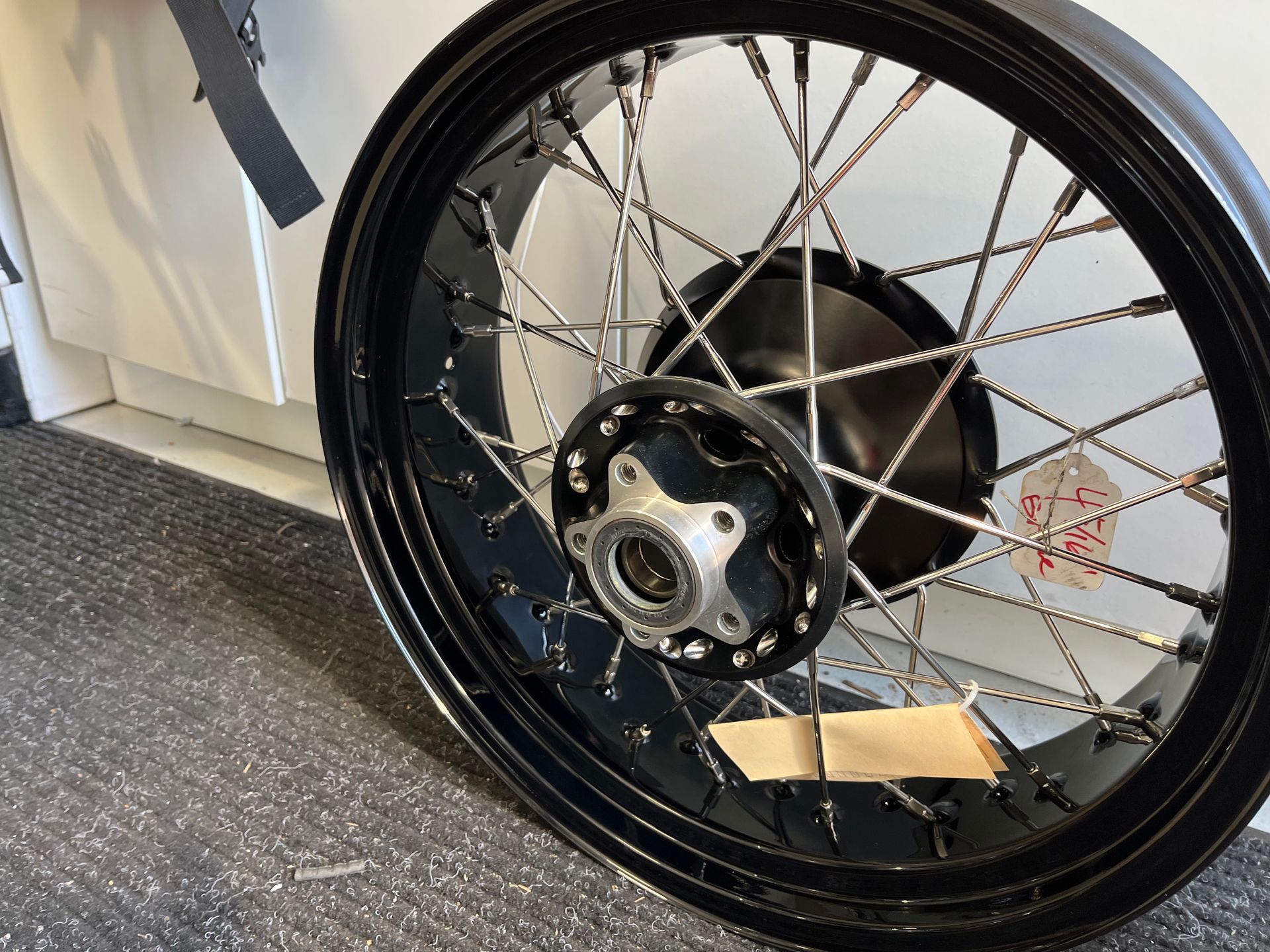 Close-up of a black motorcycle wheel with spokes and hub indoors on a carpeted floor.