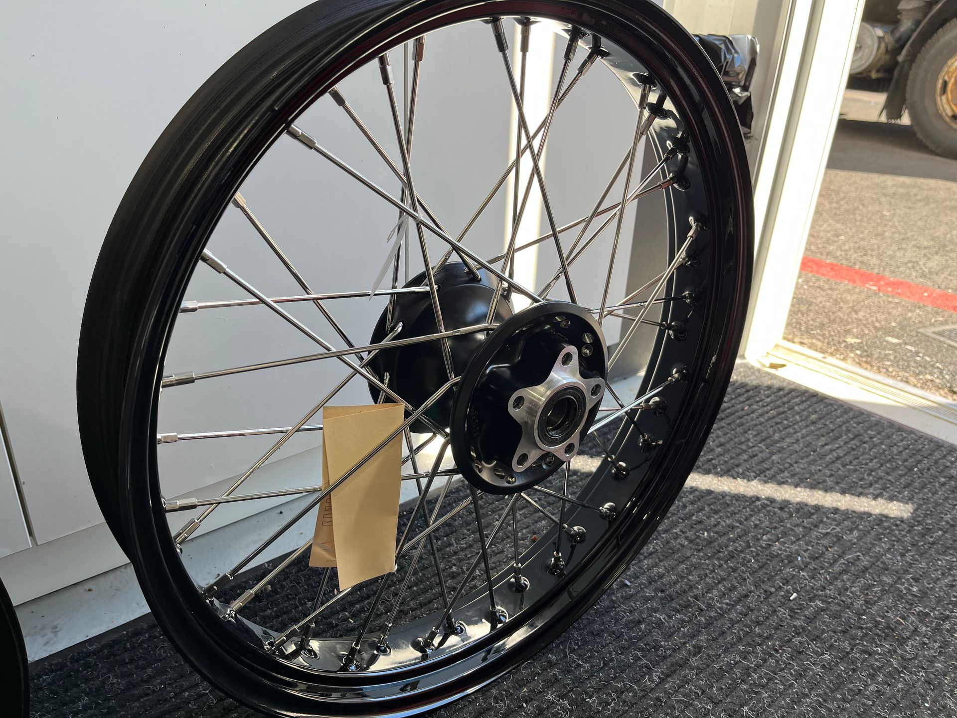 Black motorcycle wheel with silver spokes leaning against a white vehicle indoors.