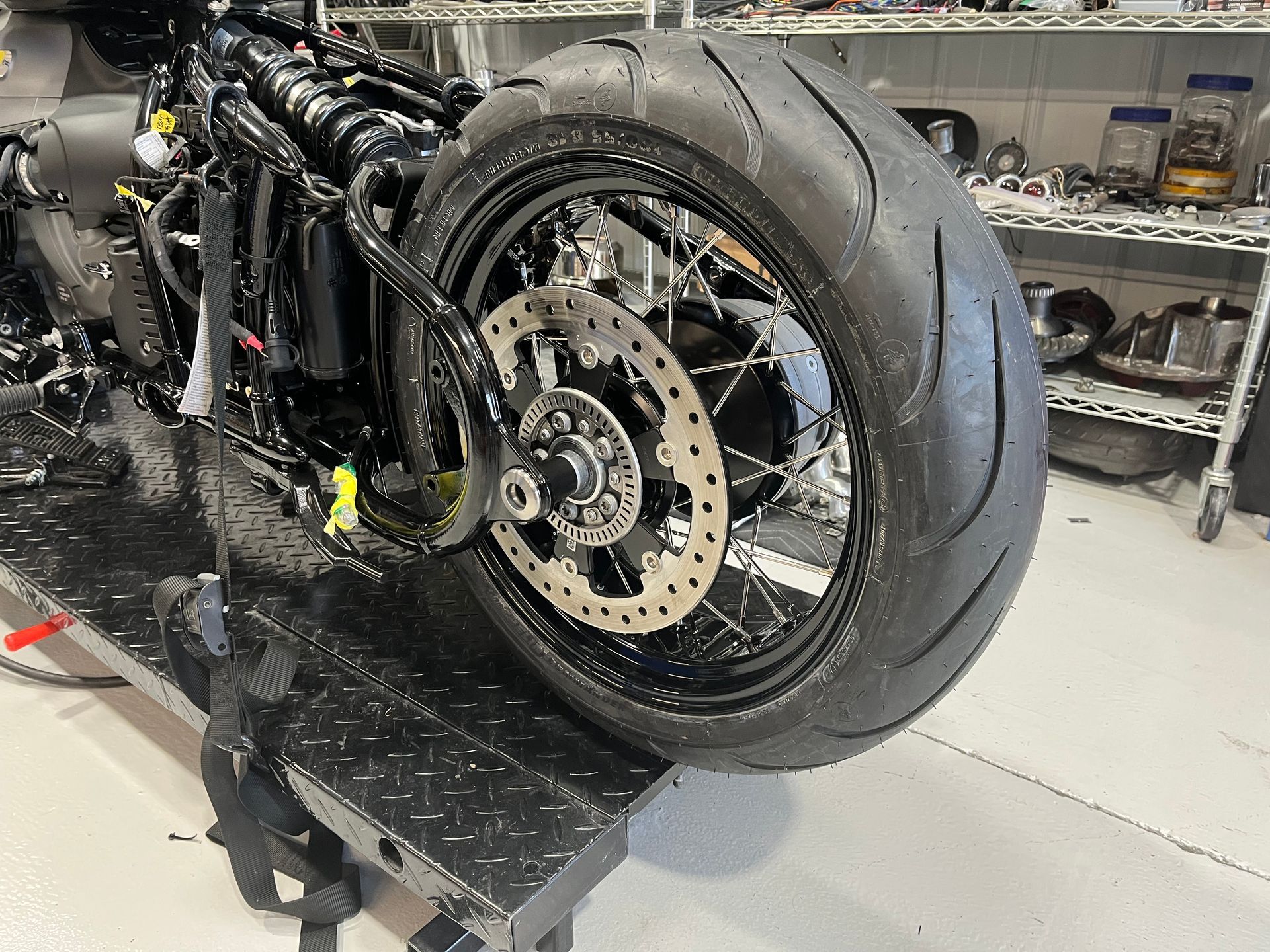 Black custom motorcycle frame with large rear tire in a workshop, viewed from the side.