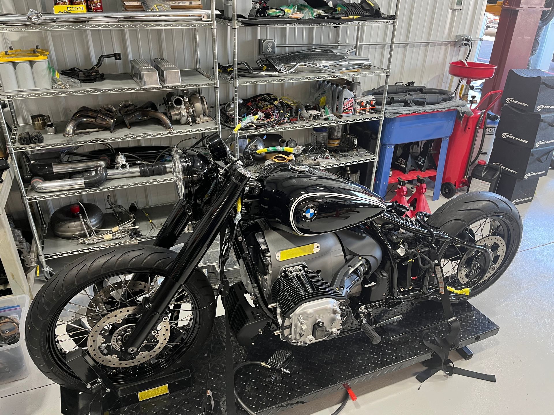 Black custom motorcycle in a workshop, with shelves of parts and tools in the background