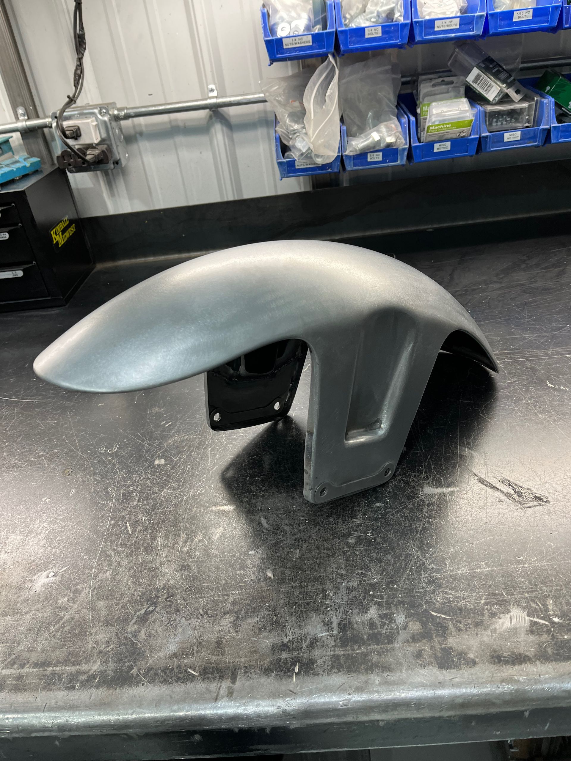 Silver motorcycle fender mounted on a black workbench in a workshop setting