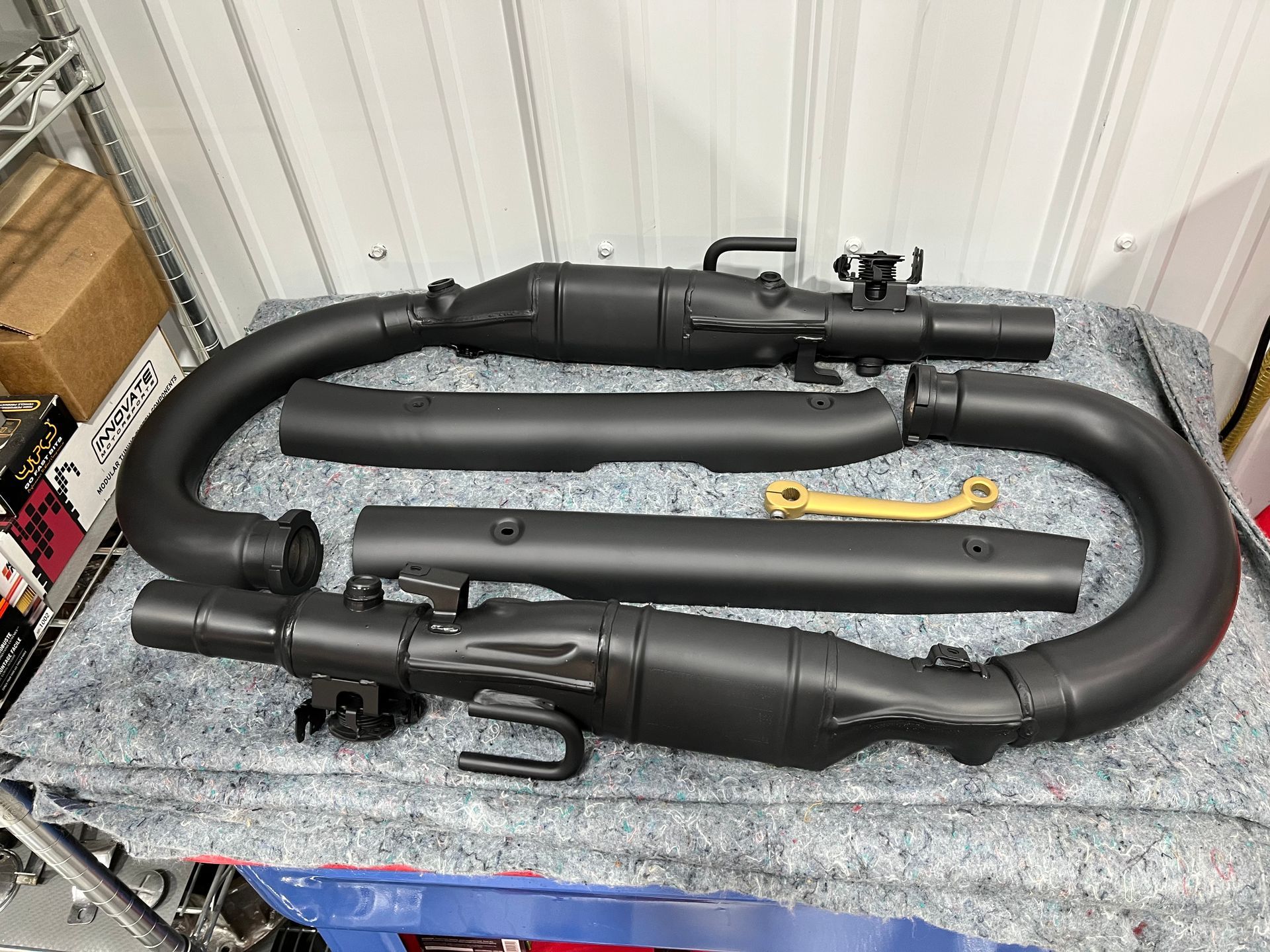 Two black motorcycle exhaust pipes with a yellow tool on a gray workbench in a garage.