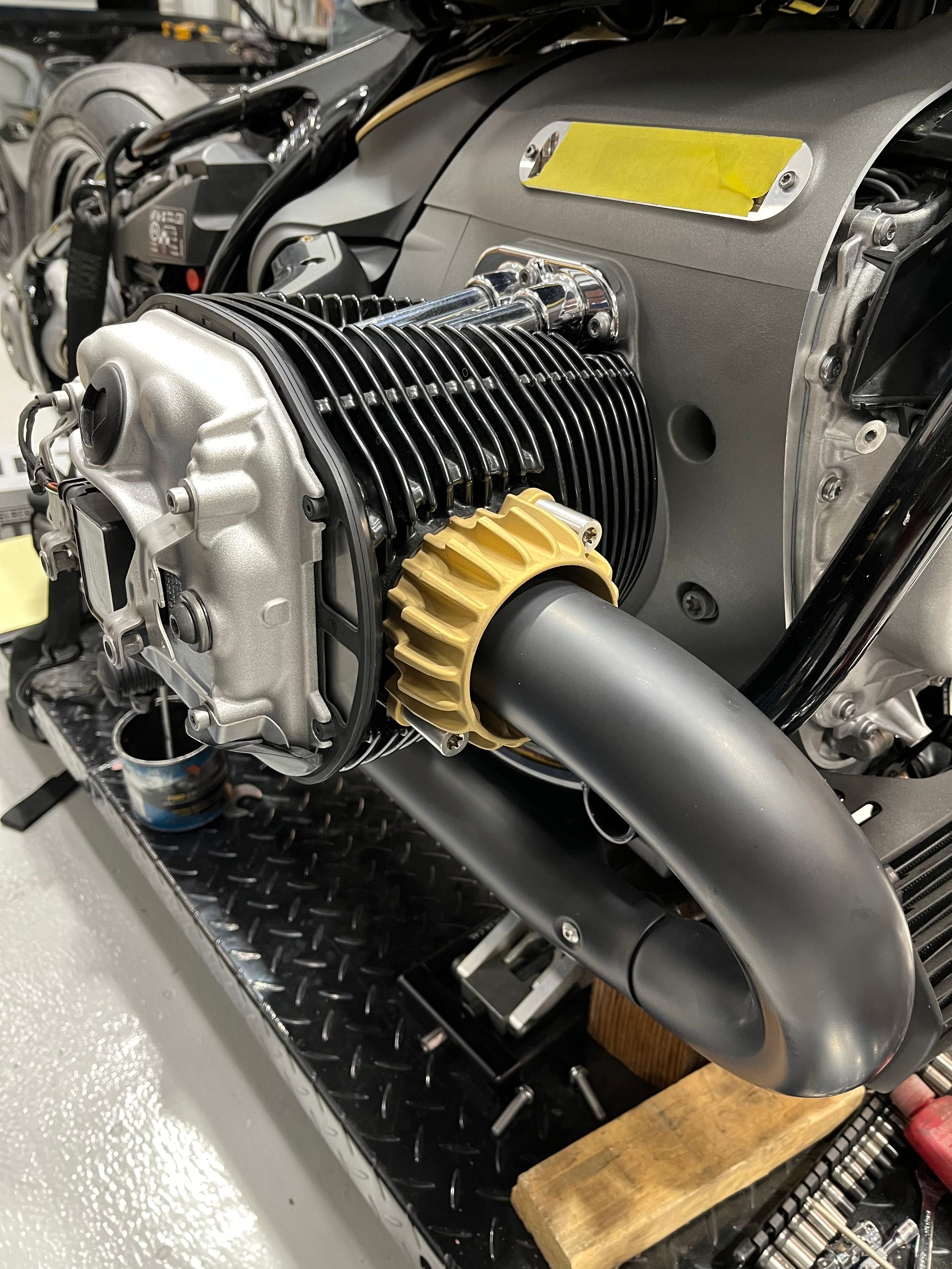 Close-up of a small engine with a black exhaust pipe and yellow intake gear on a metal surface